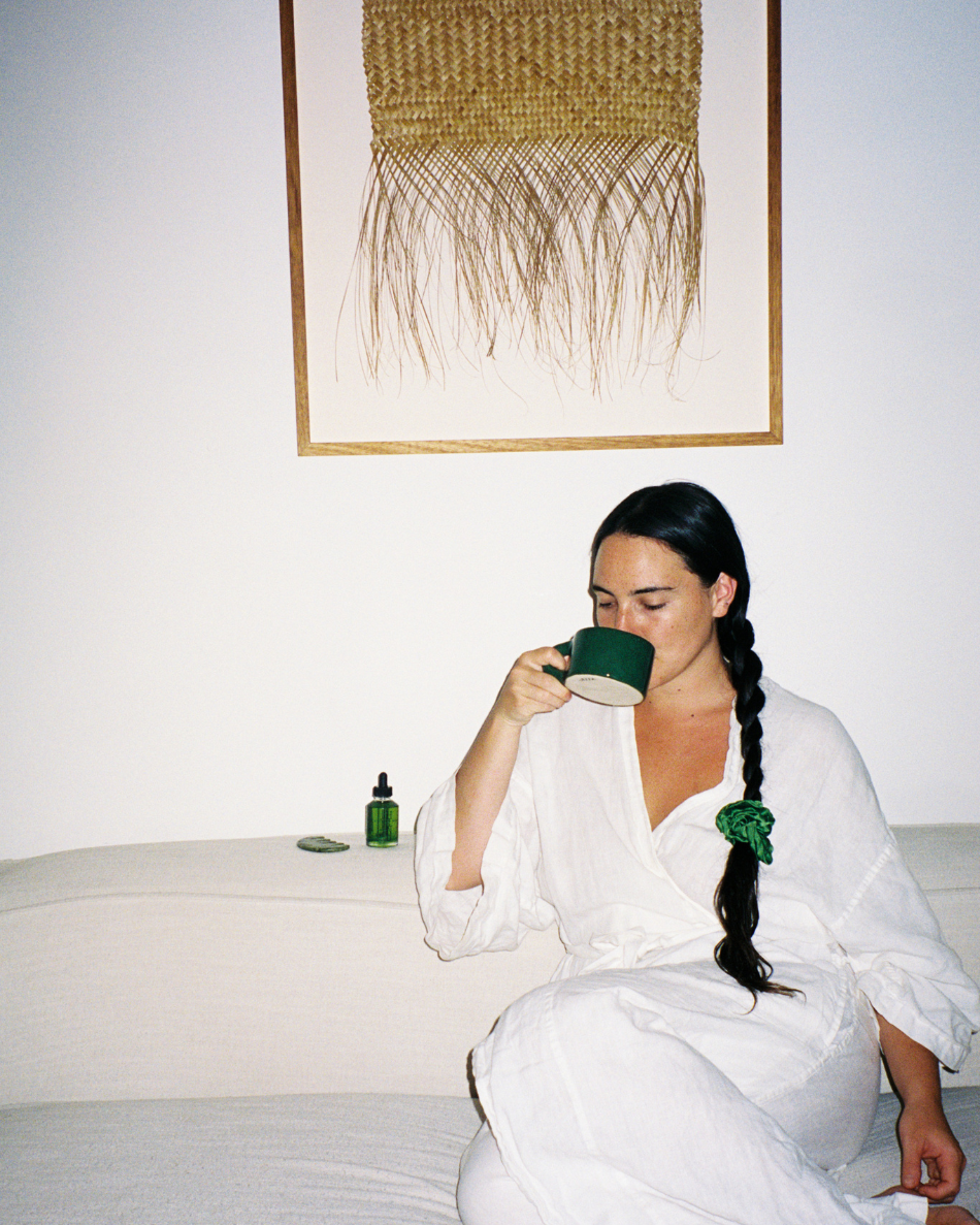 Woman in a white robe drinking from the green HINU Ritual Mug