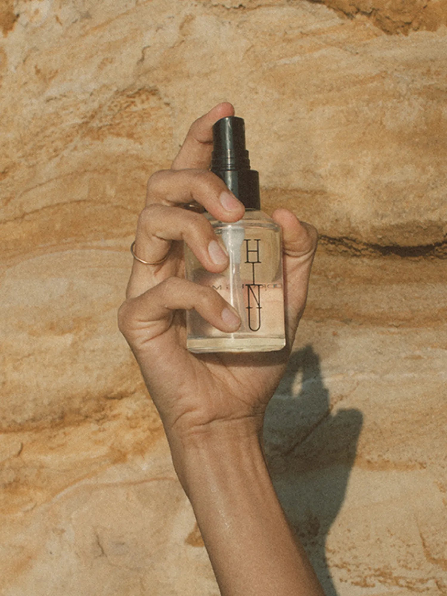 Hand holding HINU Hydrating Mist against a sunlit stone background