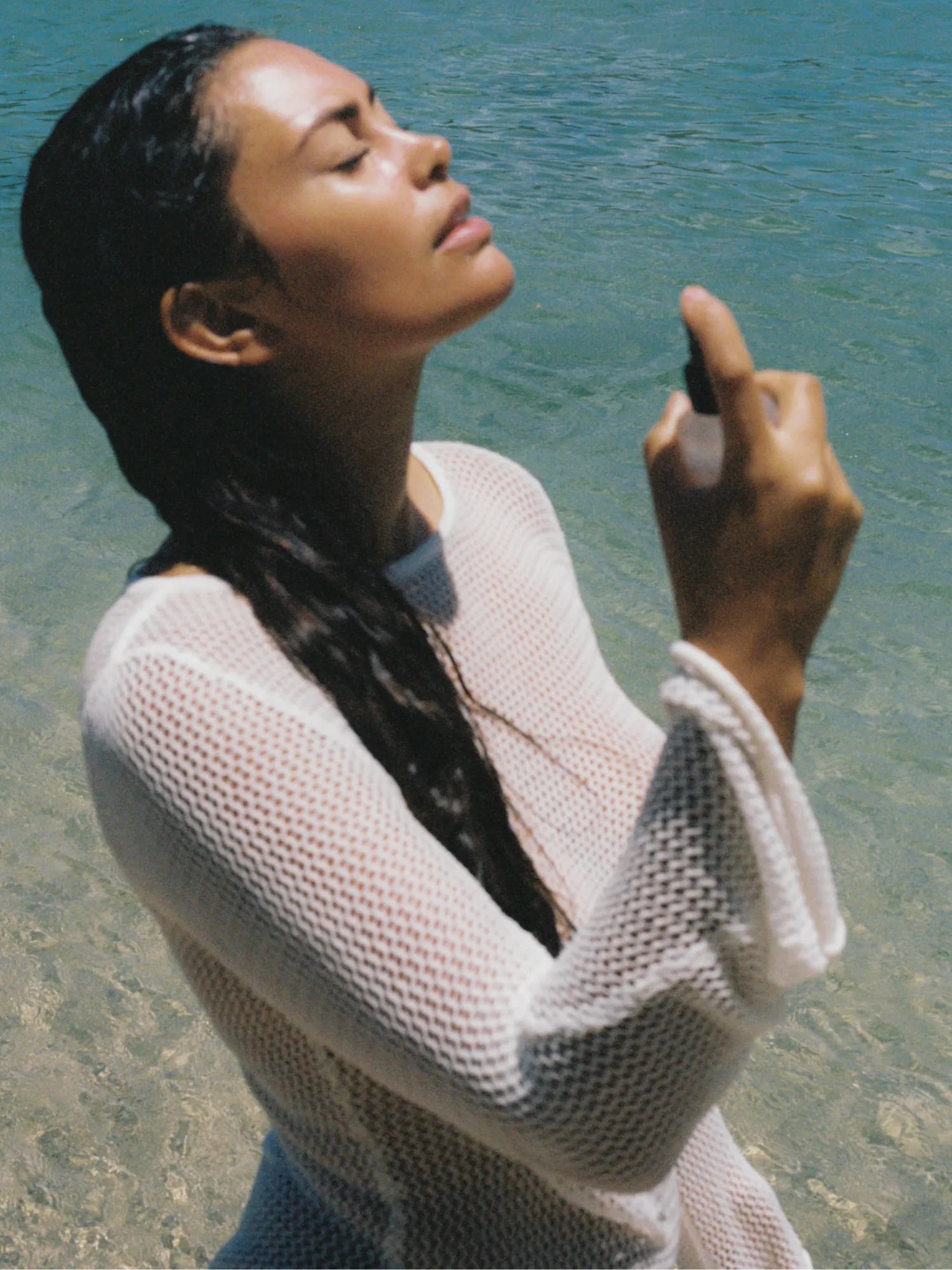 Woman spraying HINU Hydrating Mist on her face beside the ocean