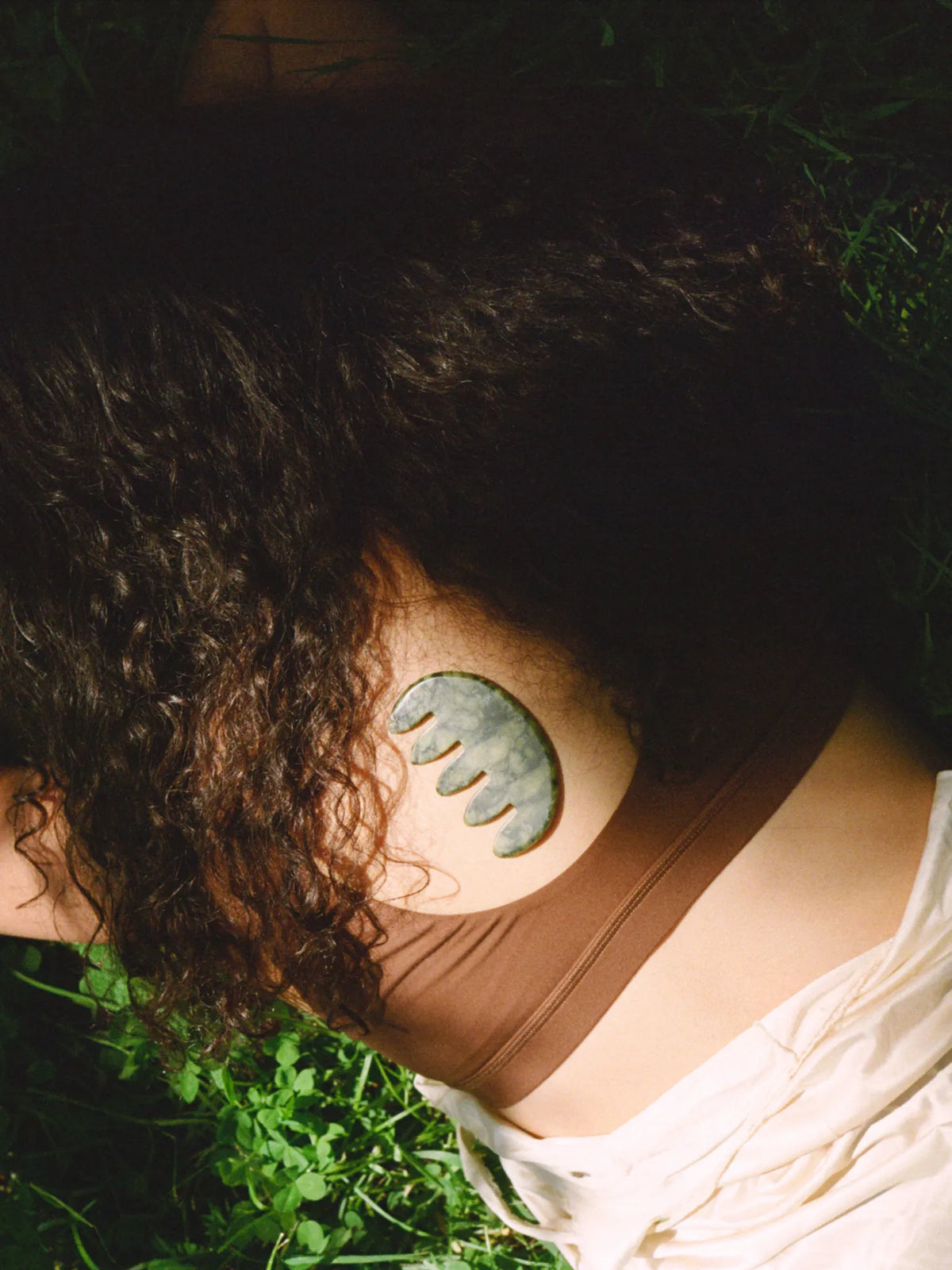 Close-up of a woman's curly hair and shoulder in dappled forest light