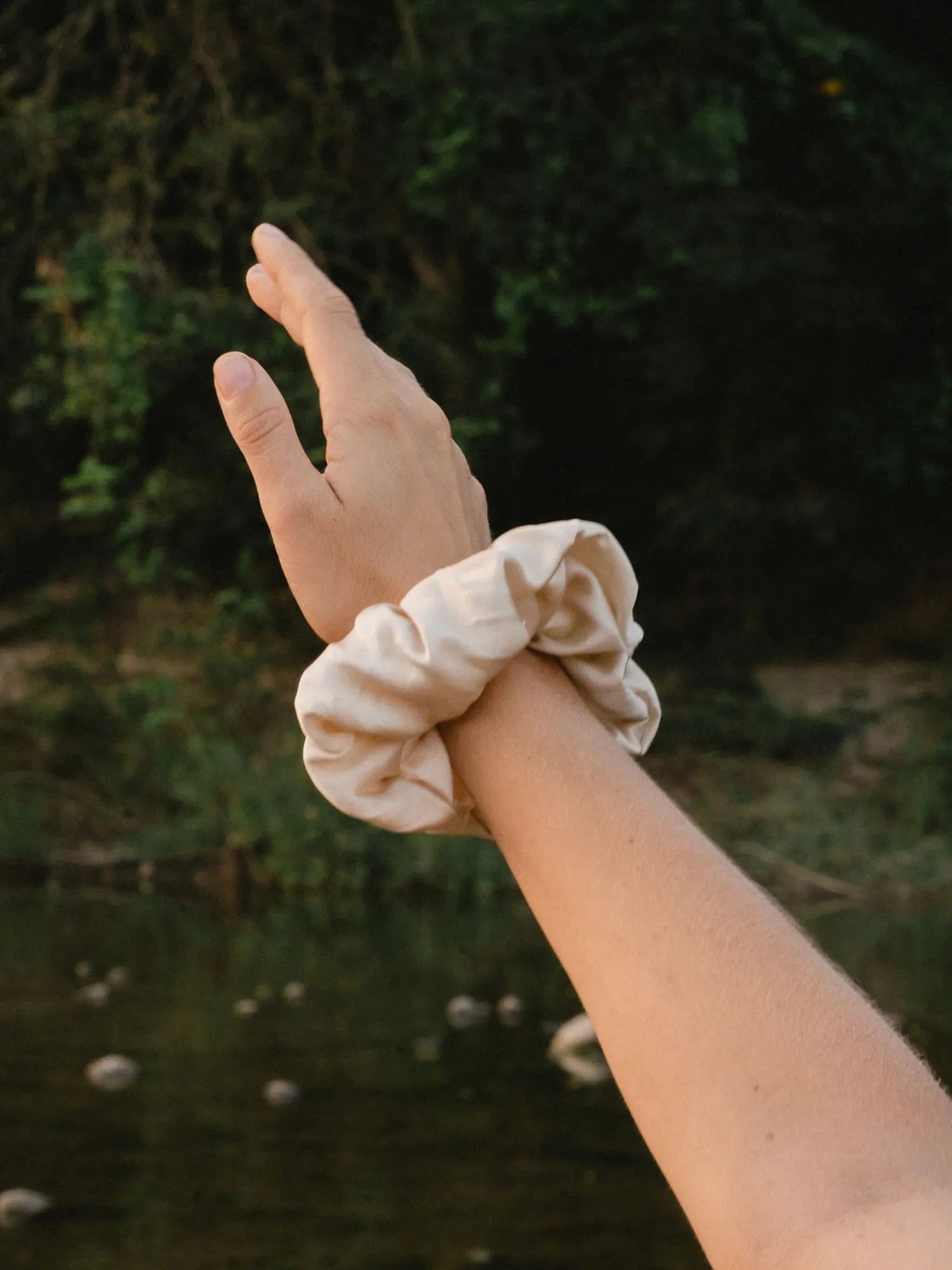 Cream HINU Silk Scrunchie worn around a wrist outdoors