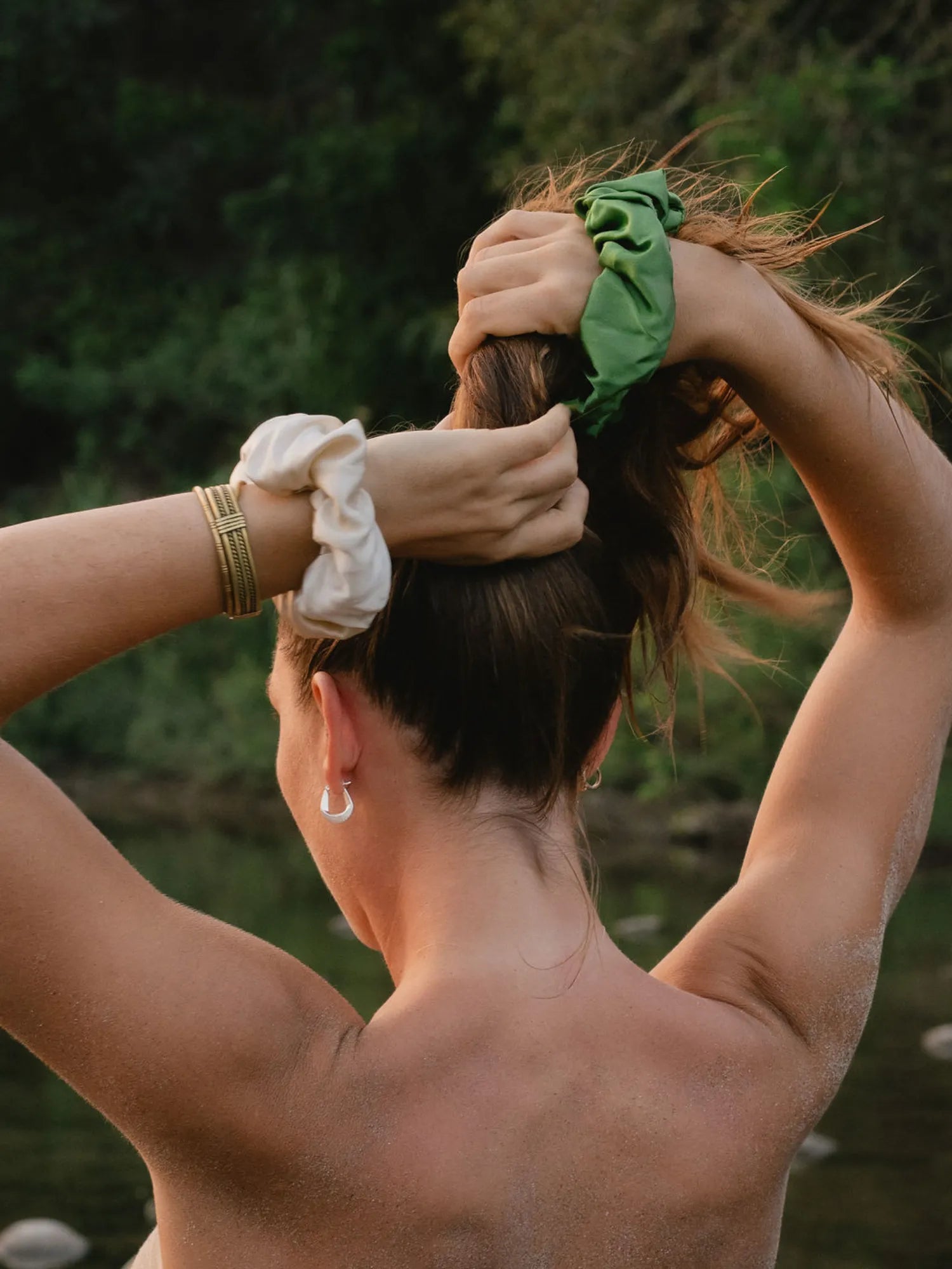 Woman tying her hair with green and cream HINU Silk Scrunchies outdoors