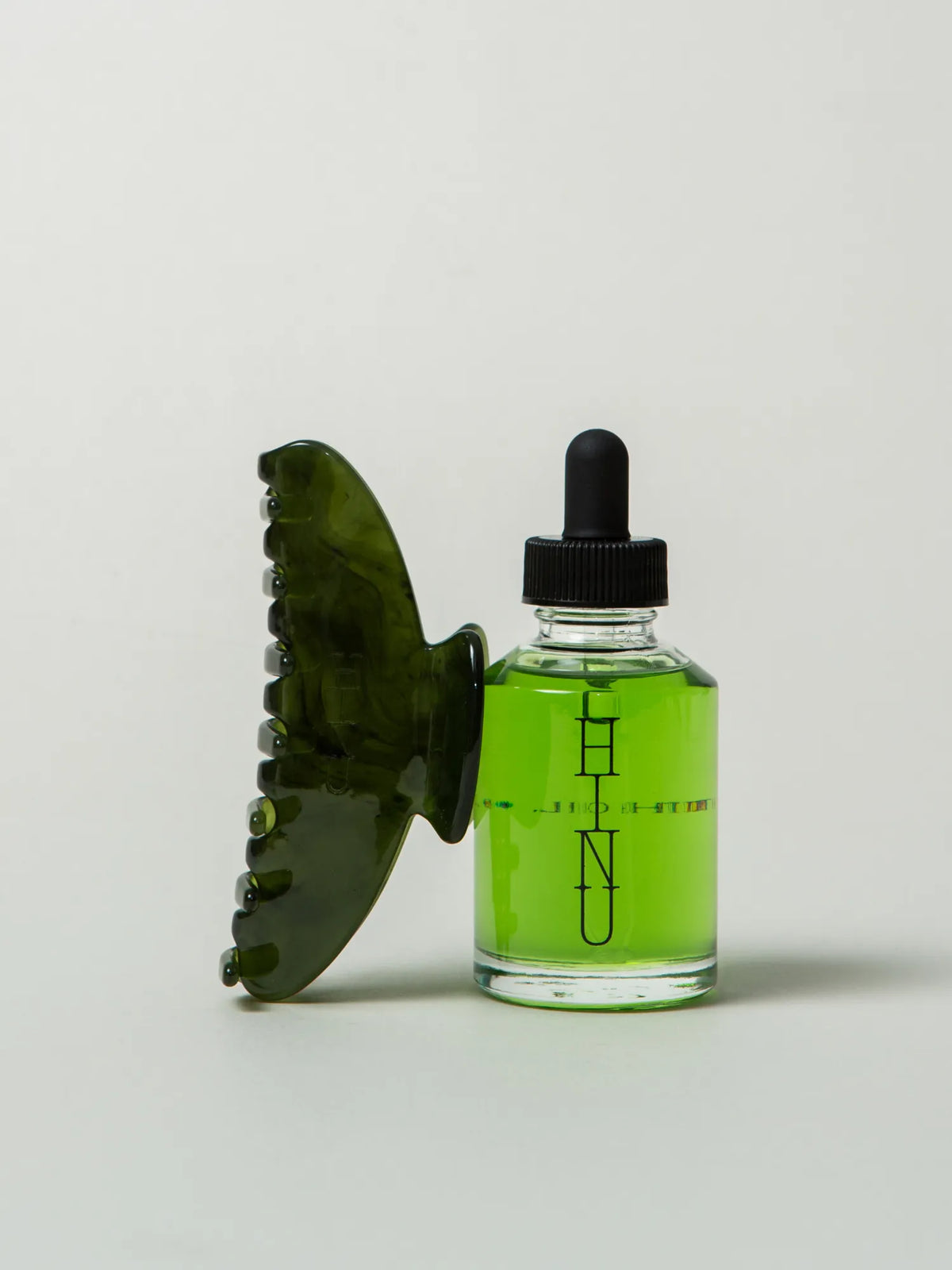 HINU Hair Growth Oil bottle beside the translucent green Rimu Claw Clip