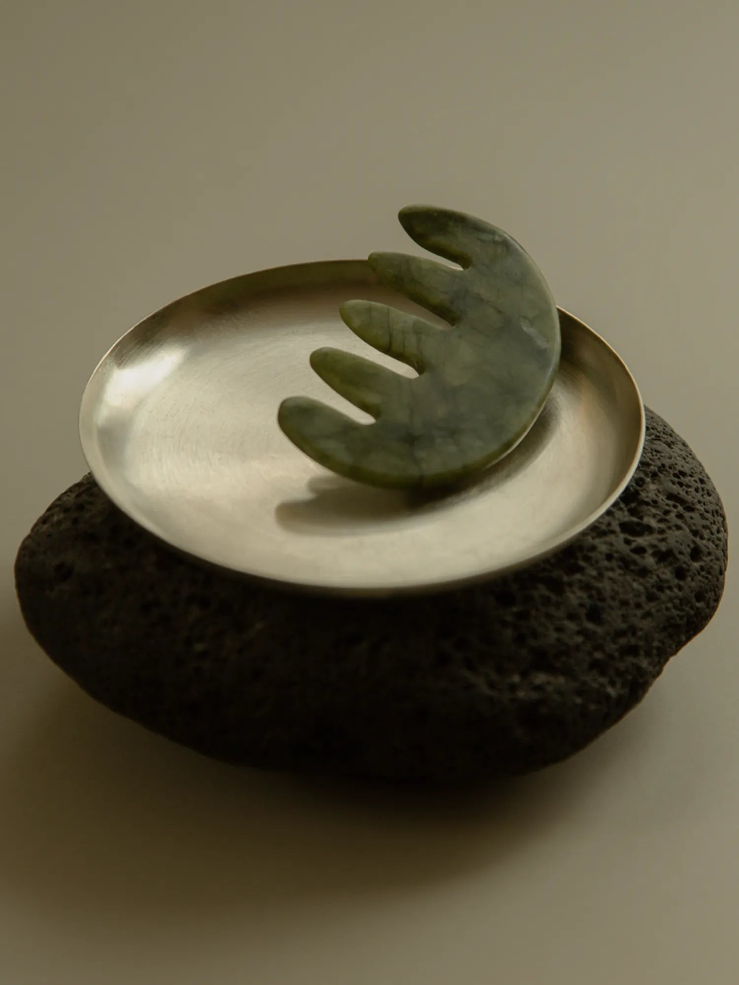 HINU Jade Scalp Stimulator displayed in a metal dish on a dark stone base