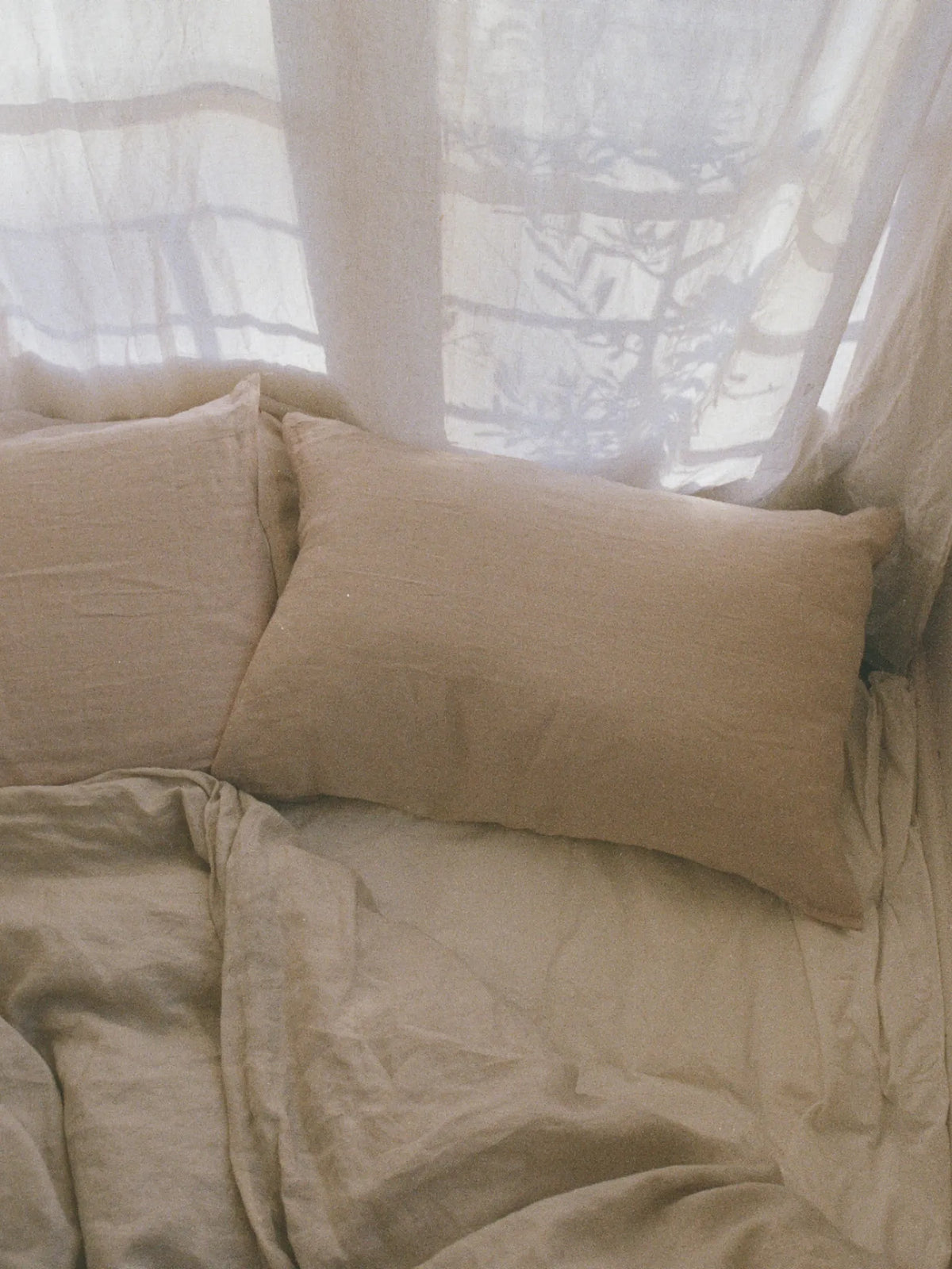 Oat-coloured HINU Hair Protect Pillowcase styled against white bedding