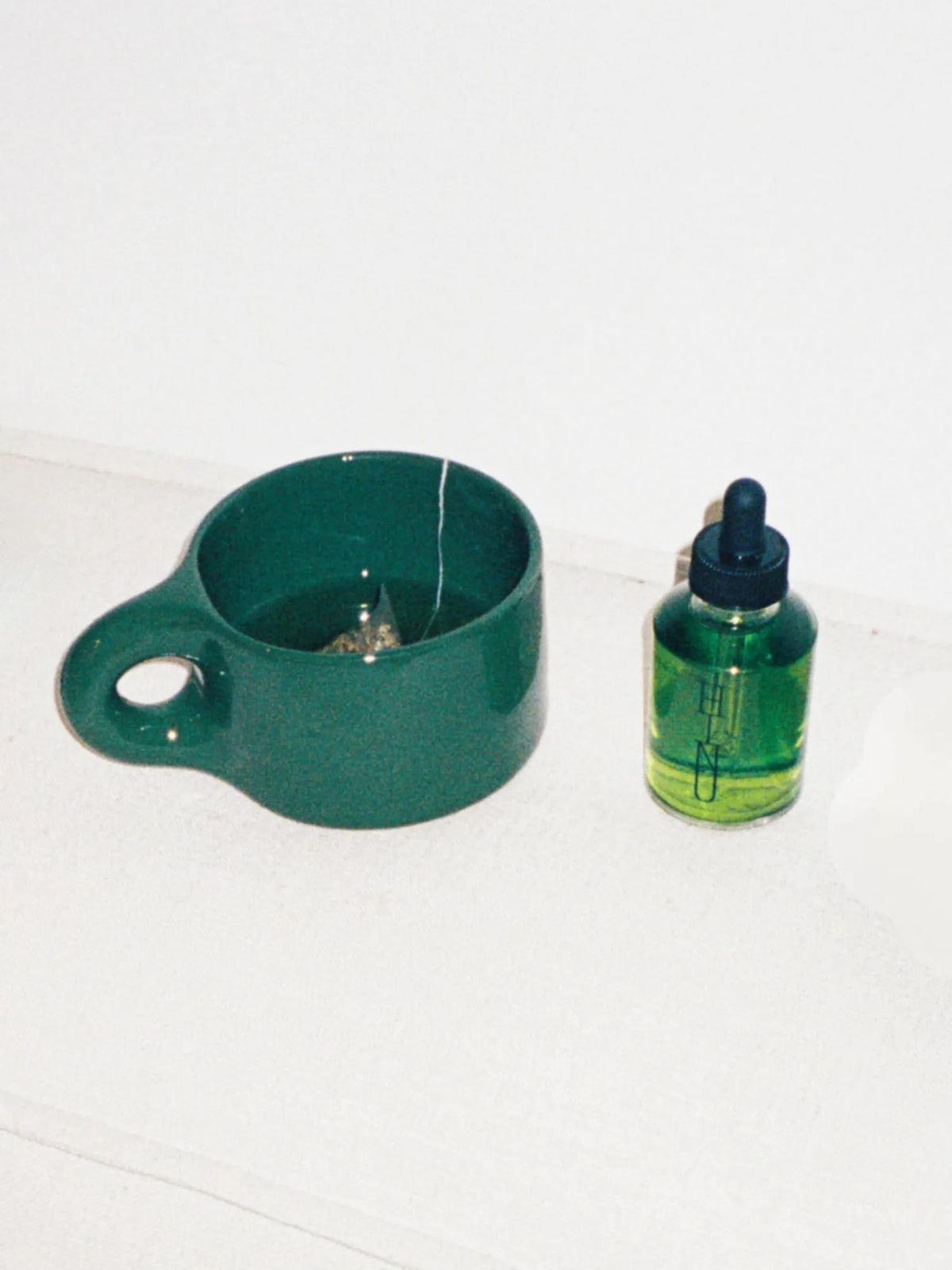 Overhead view of the green HINU Ritual Mug beside Hair Growth Oil