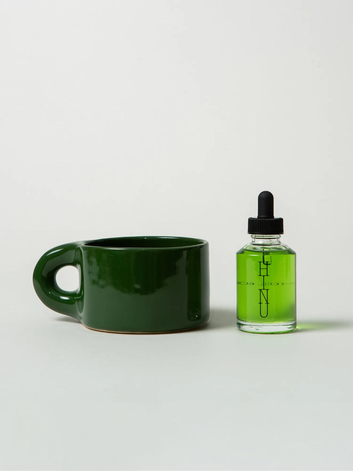 Green HINU Ritual Mug beside a bottle of Hair Growth Oil