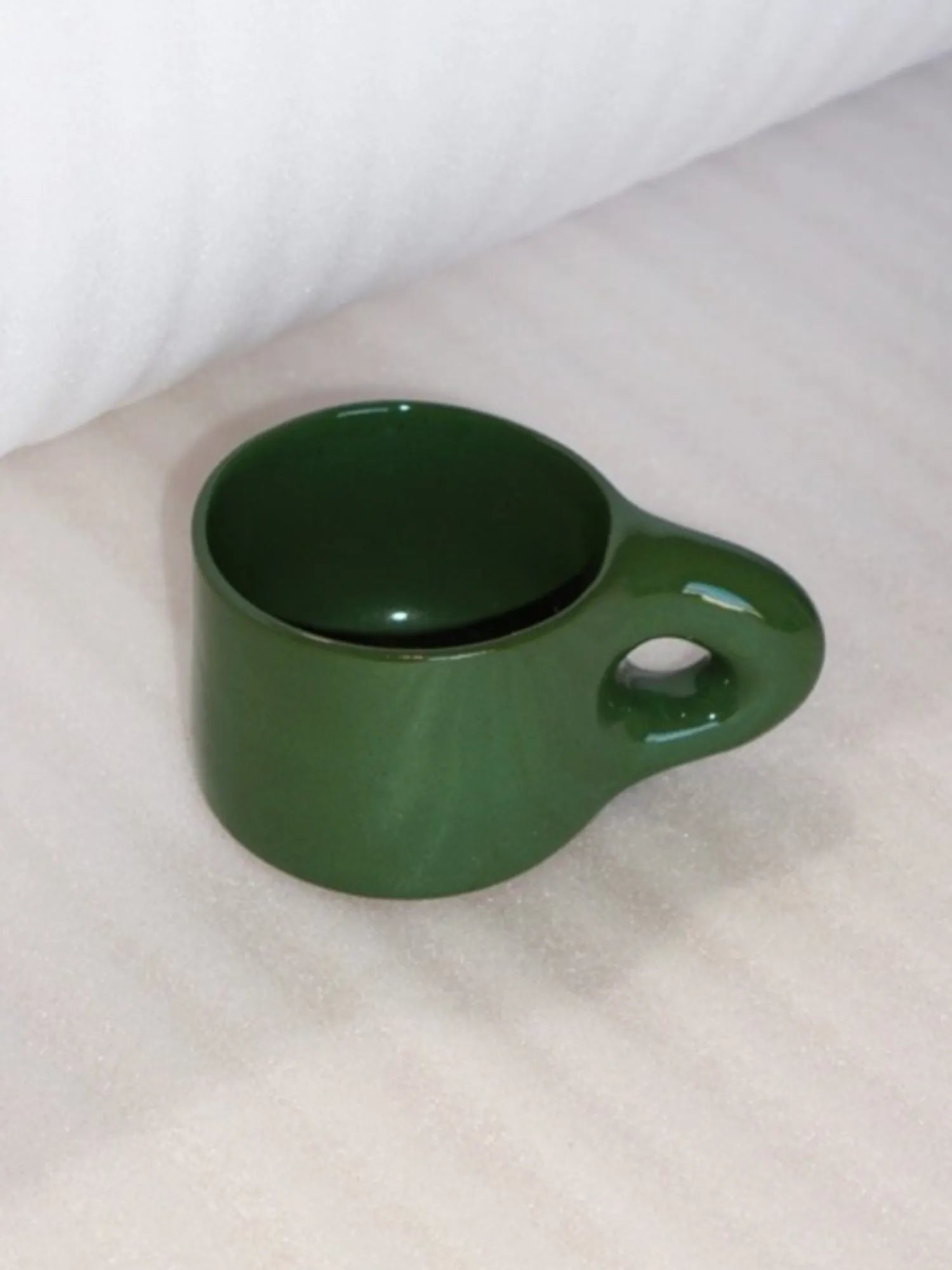 Angled view of the green HINU Ritual Mug on white fabric