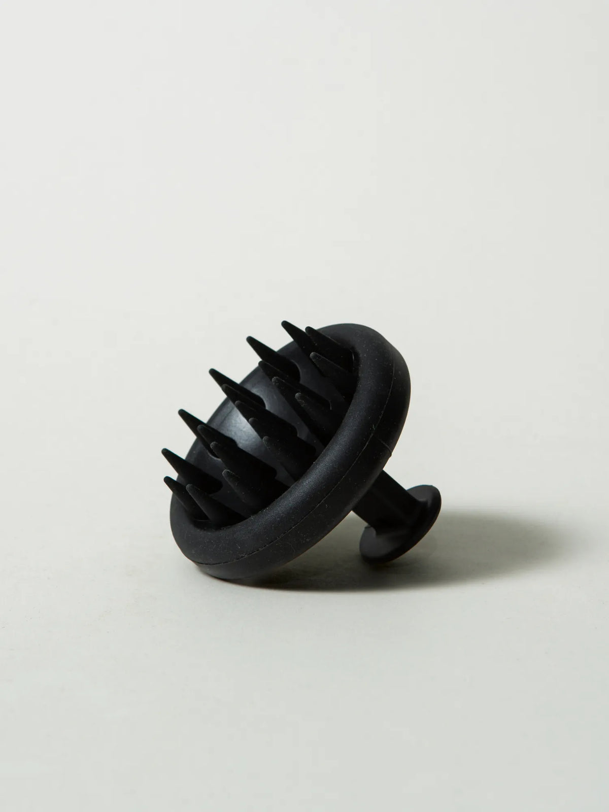 Angled view of the HINU Scalp Massager showing its bristles and hand loop