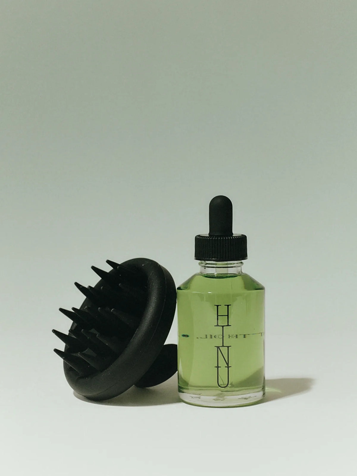 Black HINU Scalp Massager beside a bottle of Hair Growth Oil