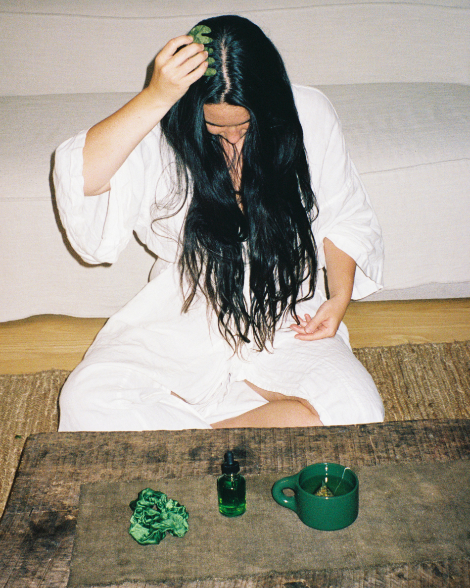 Woman applying HINU Hair Growth Oil to her scalp while seated