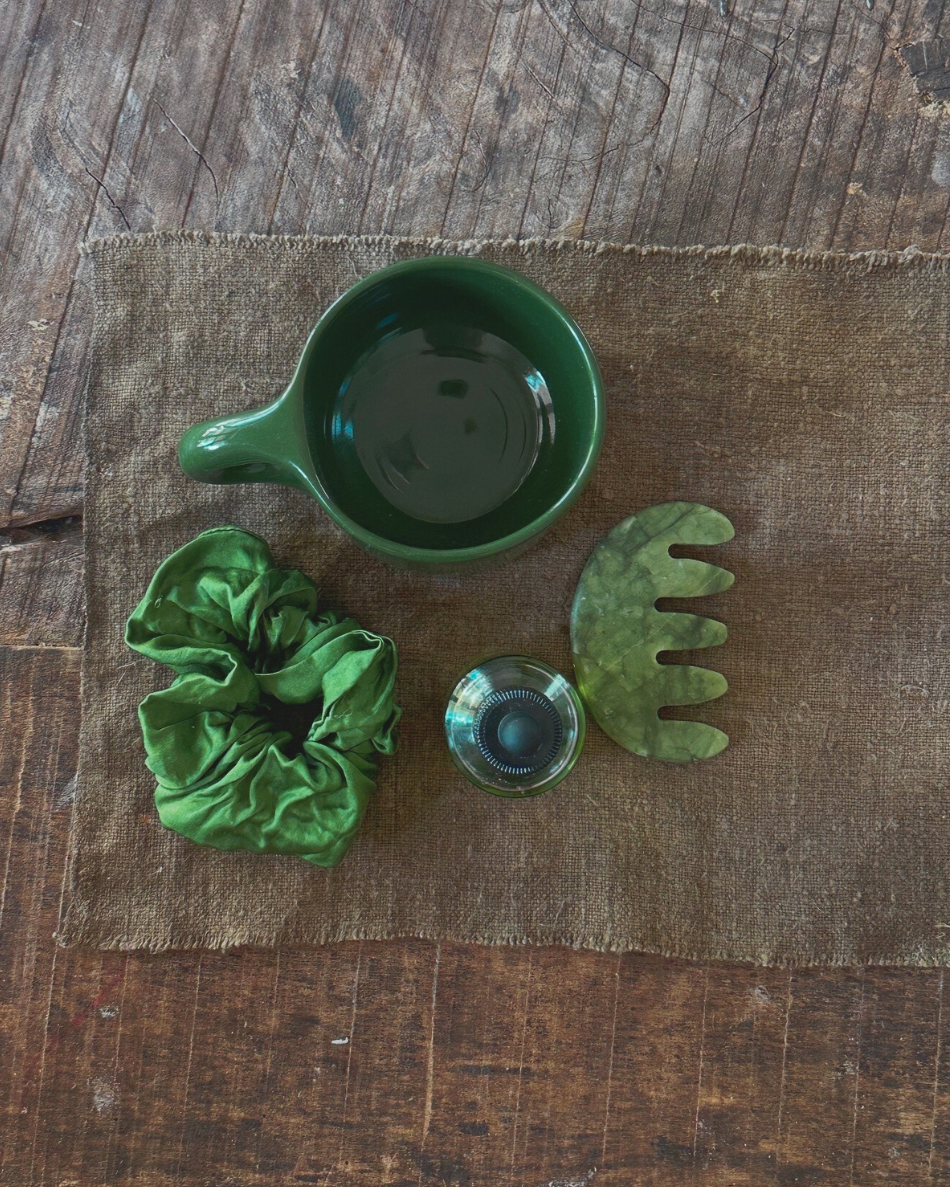 Overhead view of green Ritual Mug, scrunchie, oil bottle and jade tool