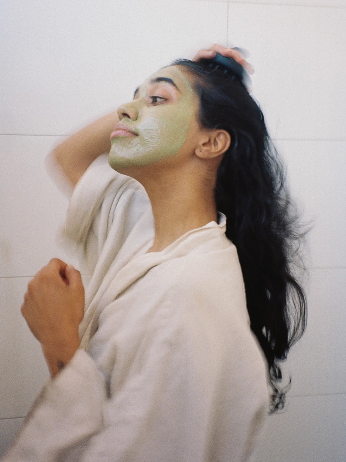 Woman wearing green Matcha Mask while massaging her wet hair