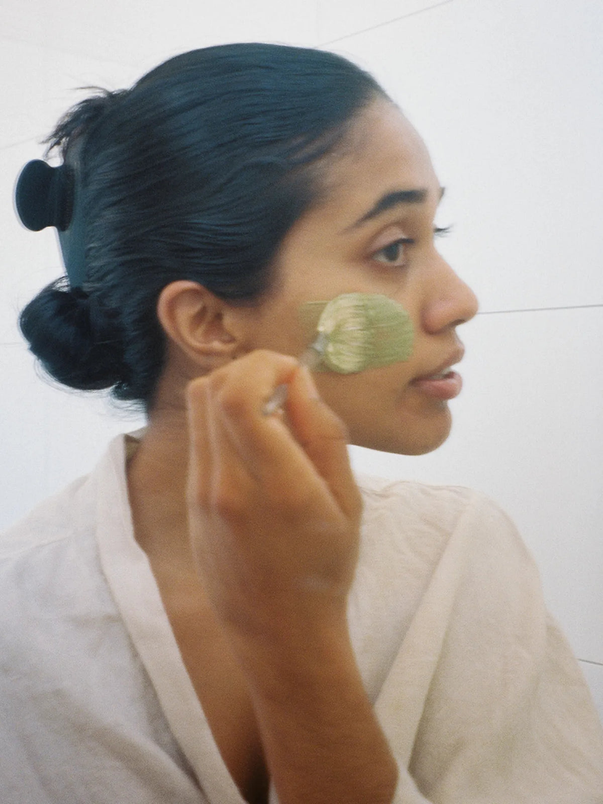 Woman applying green HINU Matcha Mask to her cheek