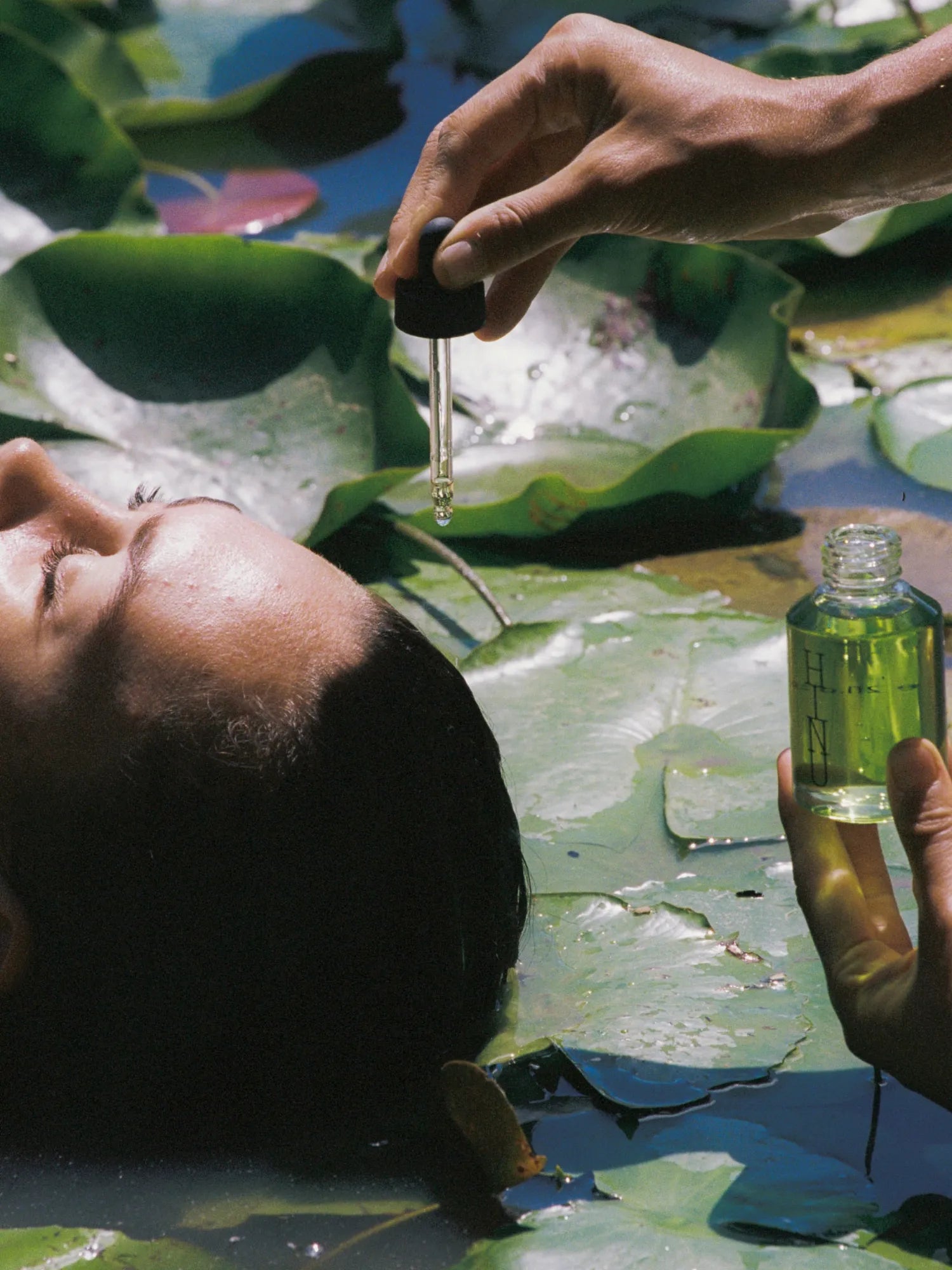 Woman applying HINU Hair Growth Oil with a dropper while floating among lily pads
