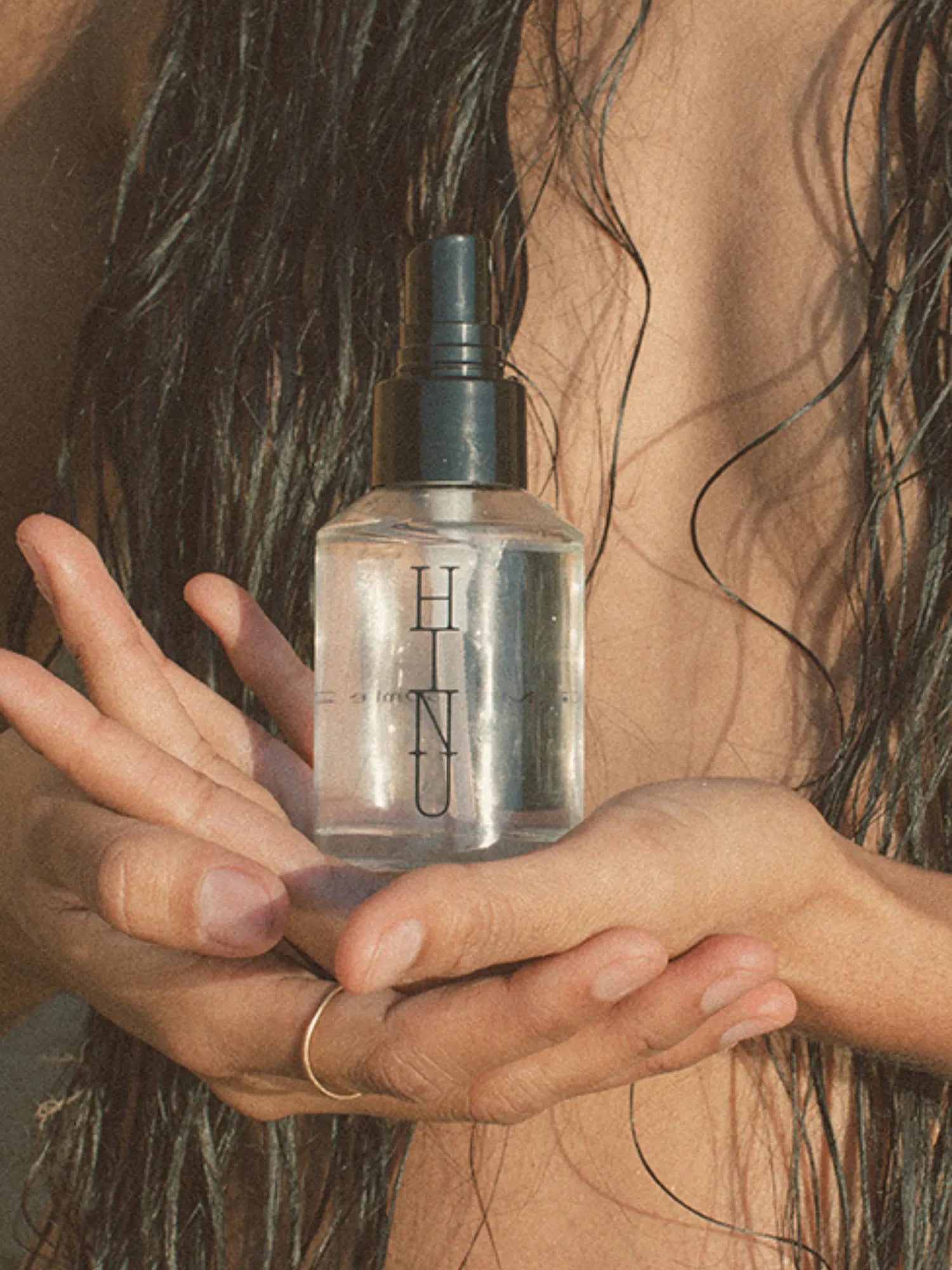 Woman holding HINU Hydrating Mist in front of her wet hair