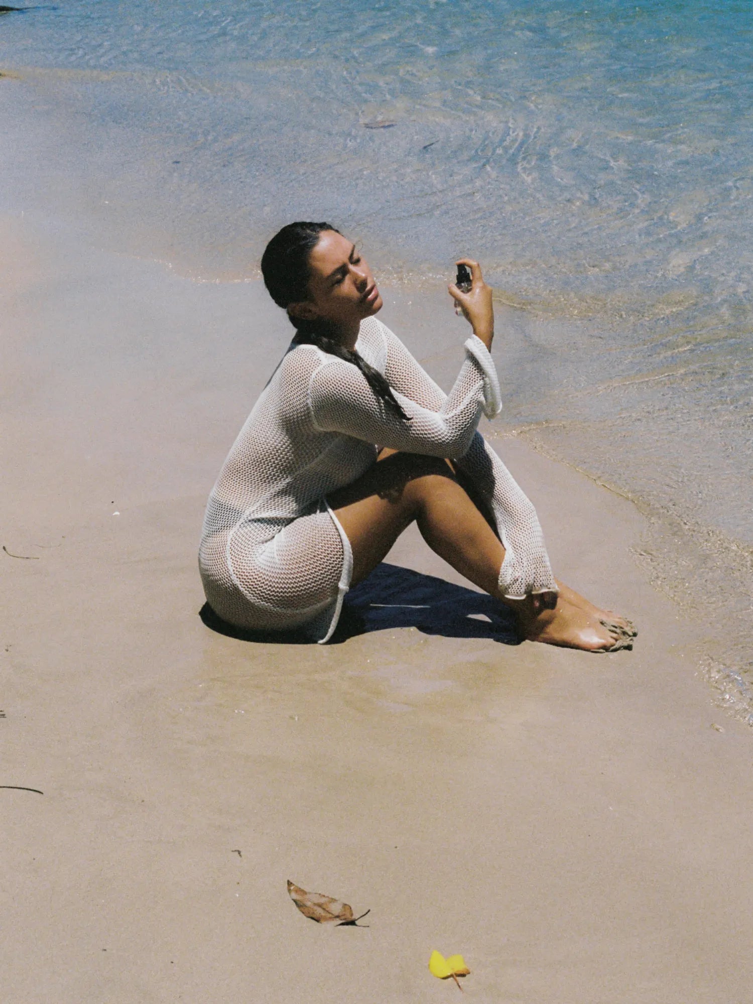 Woman holding HINU Hydrating Mist while seated beside the ocean