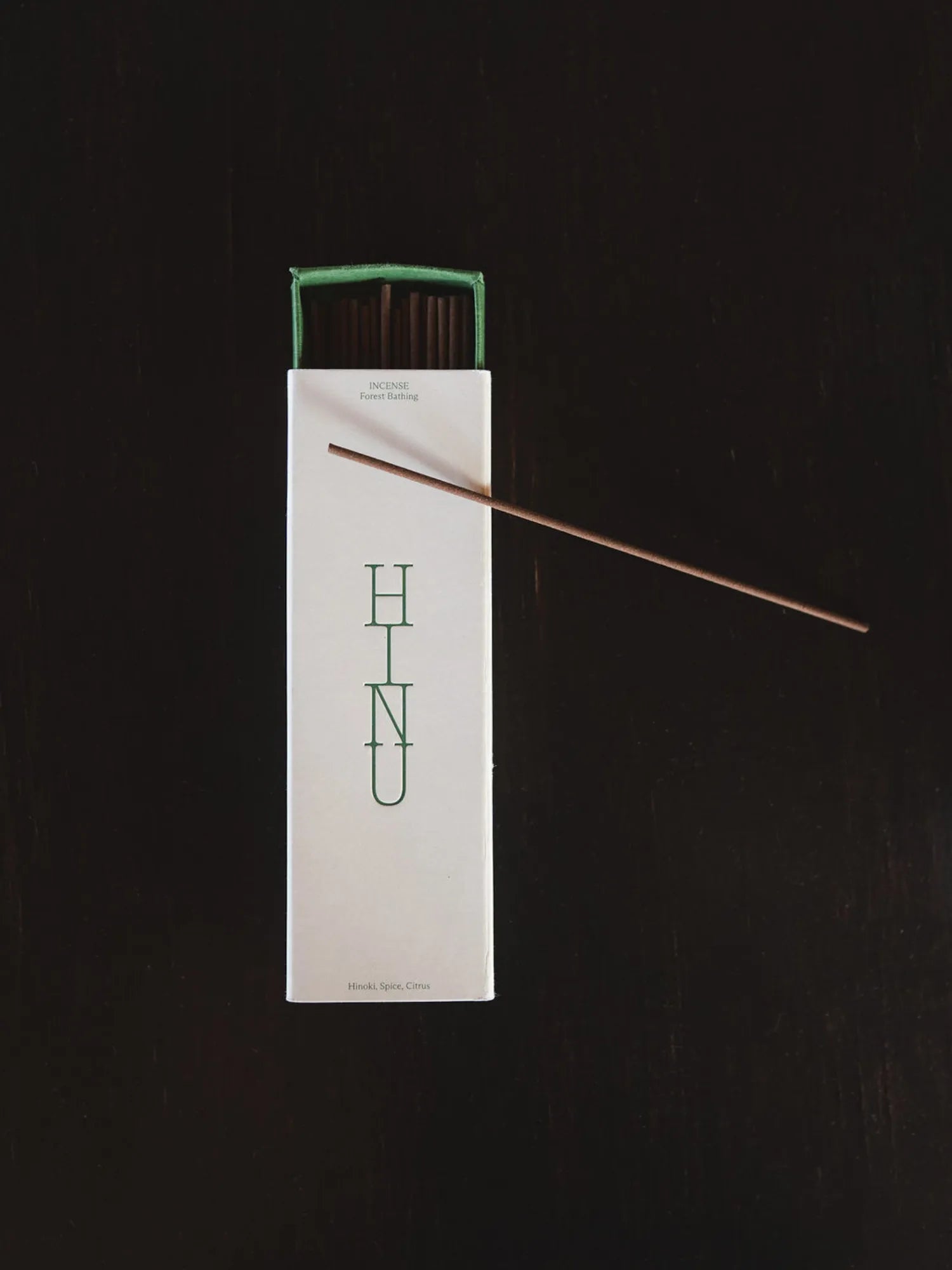 Single incense stick extending from an open HINU box on a dark background
