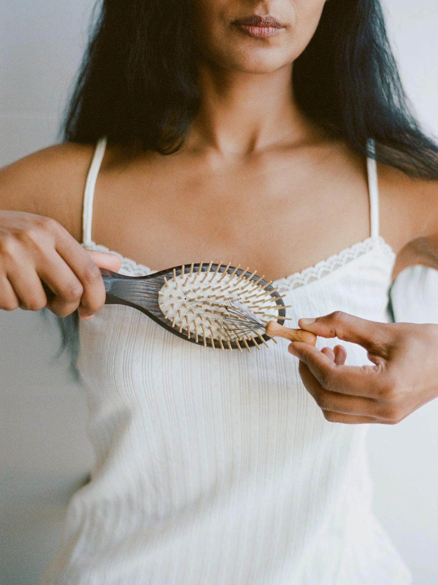 Woman holding the HINU Wooden Hair Brush across a white top