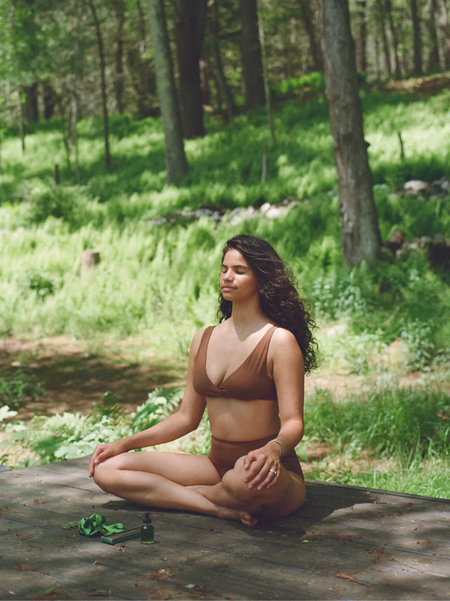 Woman meditating on a wooden deck in a forest with the ritual kit beside her