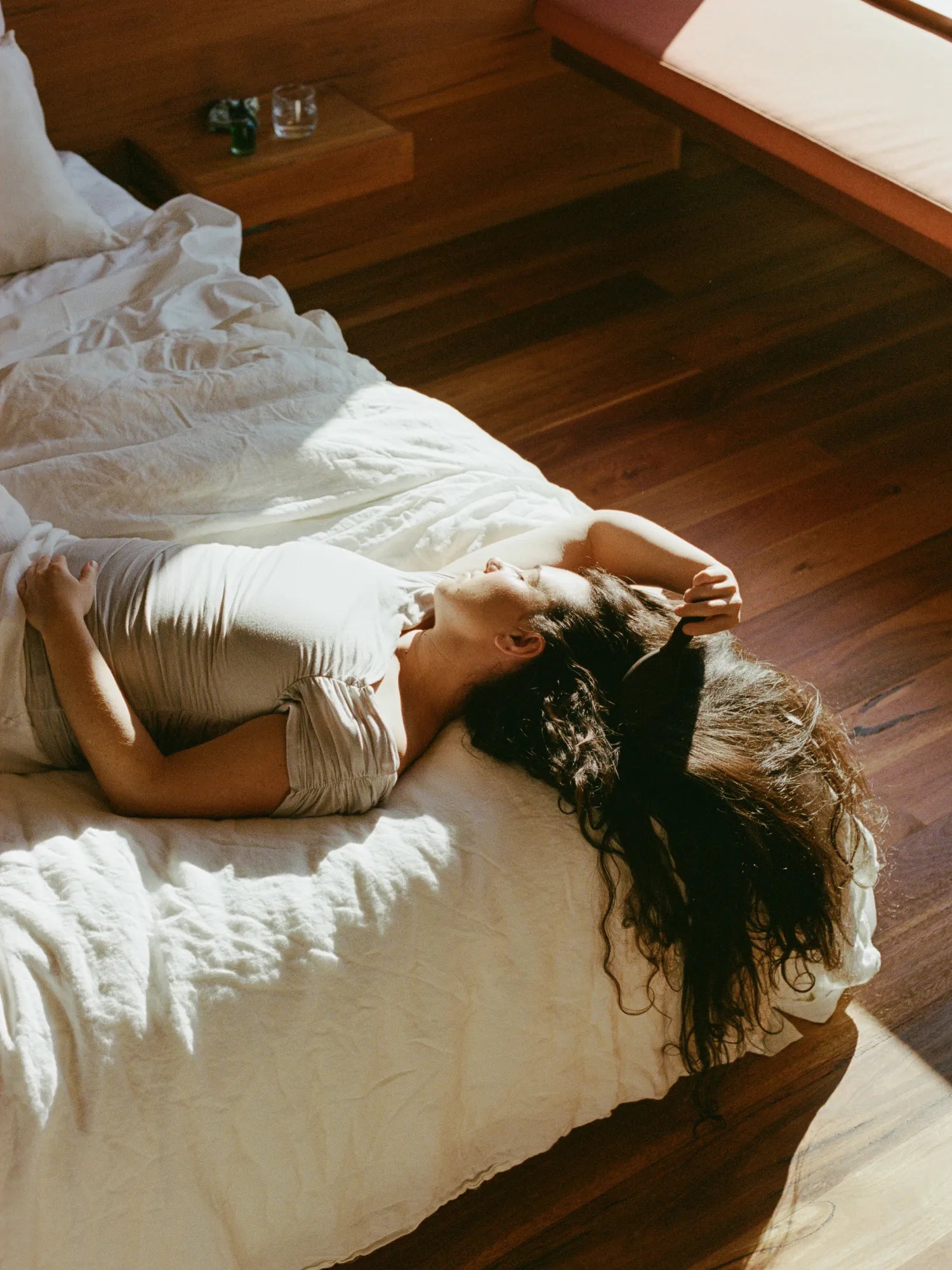 Woman reclining on a bed with long curly hair spread beside her