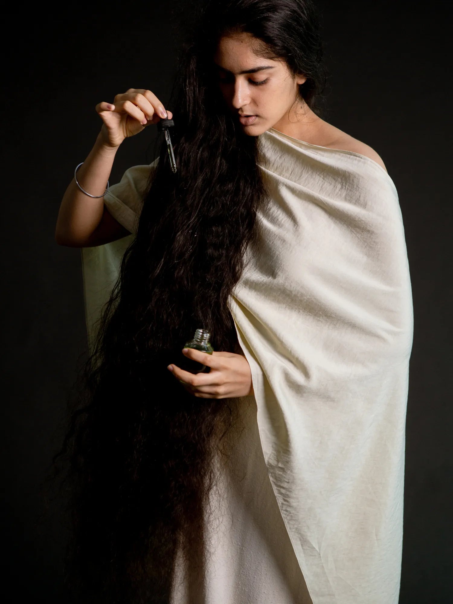 Woman applying HINU Hair Growth Oil with a dropper to her long dark hair