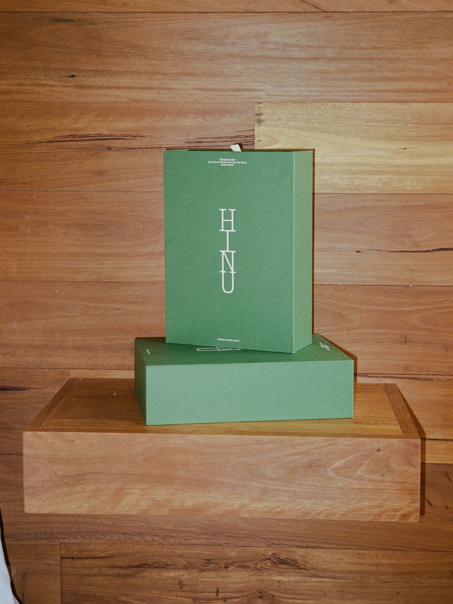 Closed green HINU Brush Gift Set boxes displayed on a wooden table