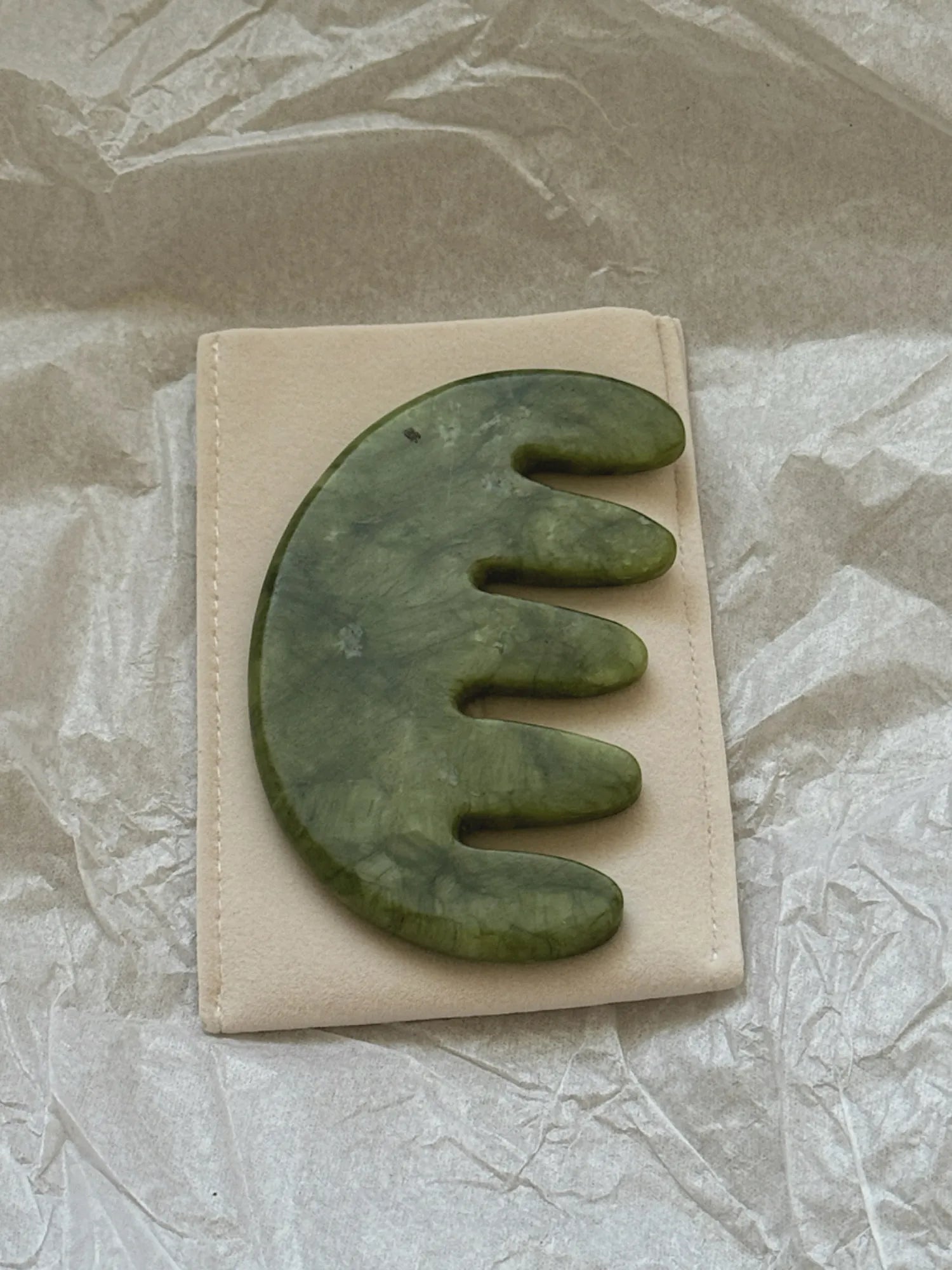 HINU Jade Scalp Stimulator resting on its cream storage pouch