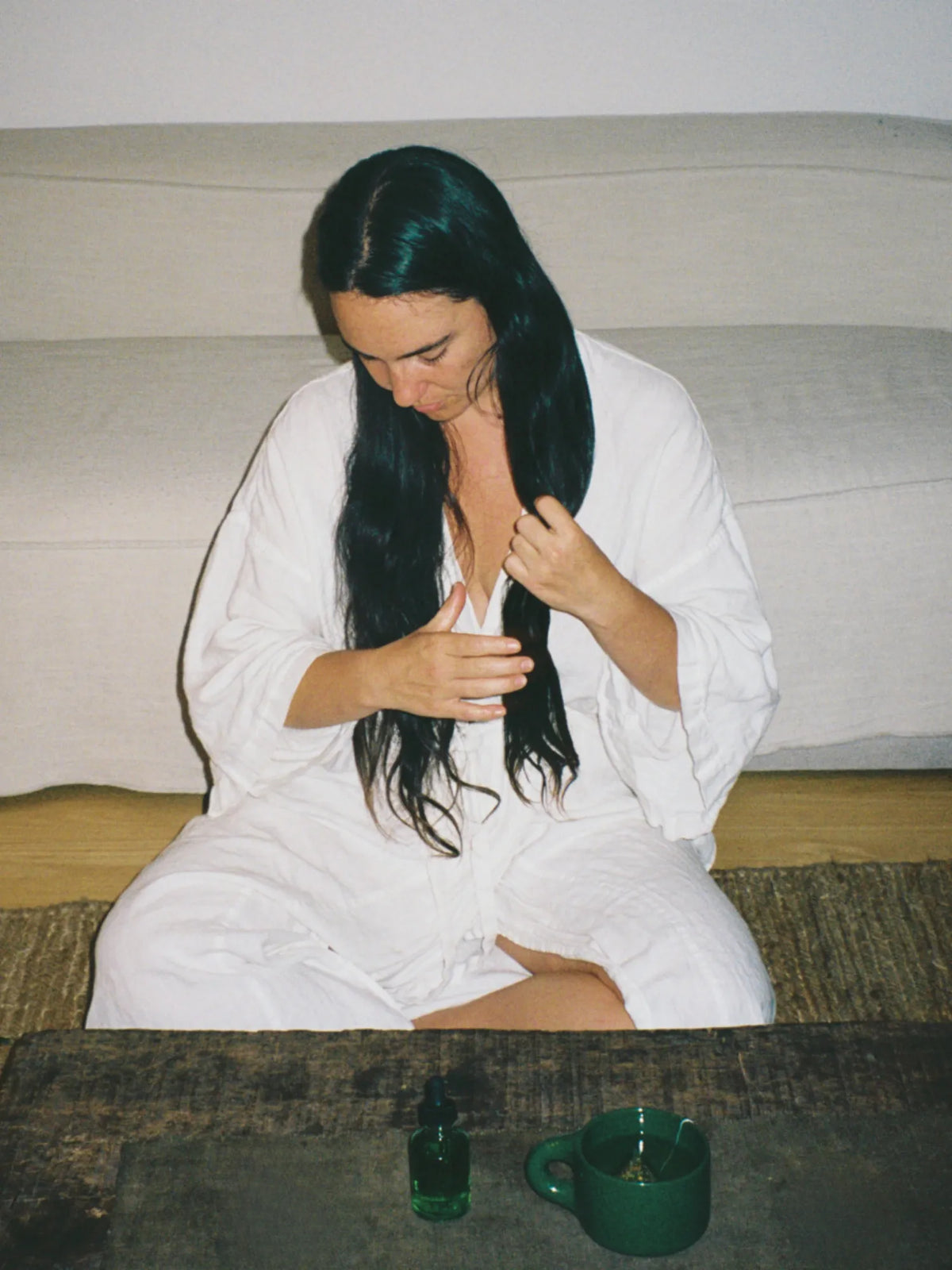 Woman applying HINU Hair Growth Oil while seated beside the Ritual Mug