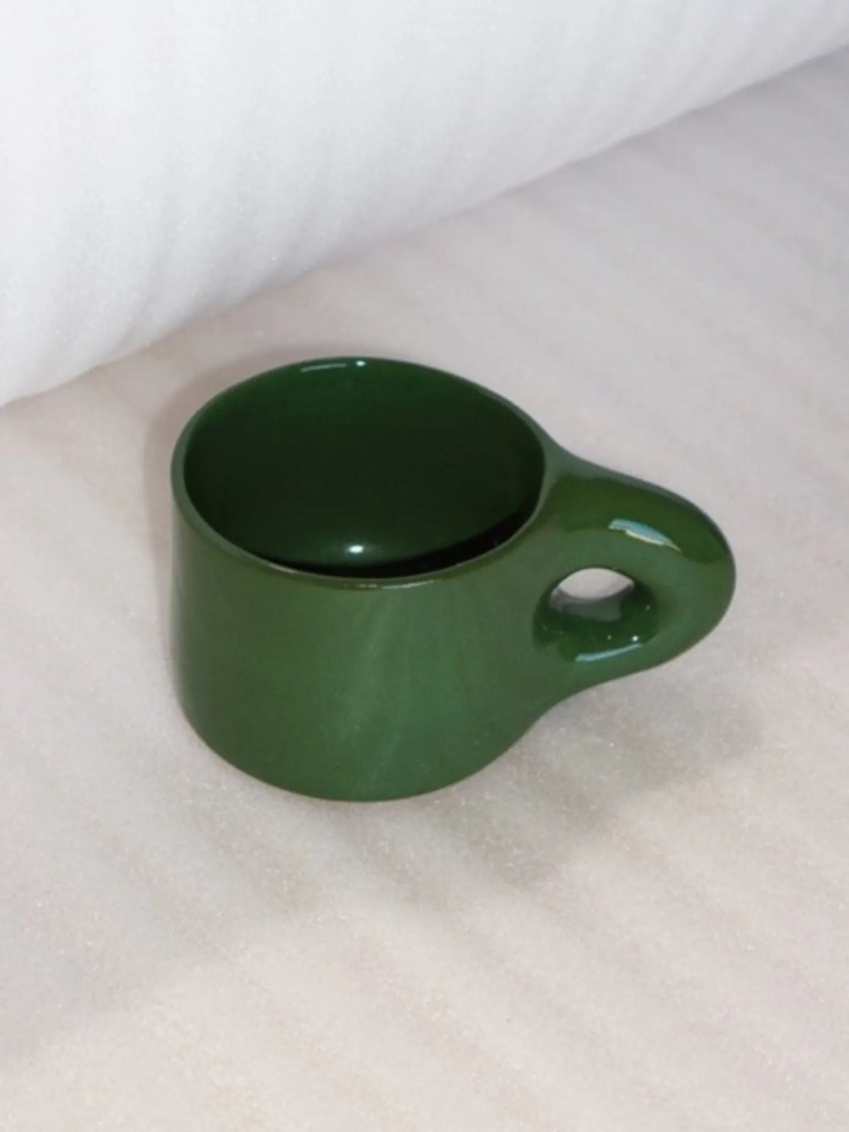 Angled view of the green HINU Ritual Mug on white fabric