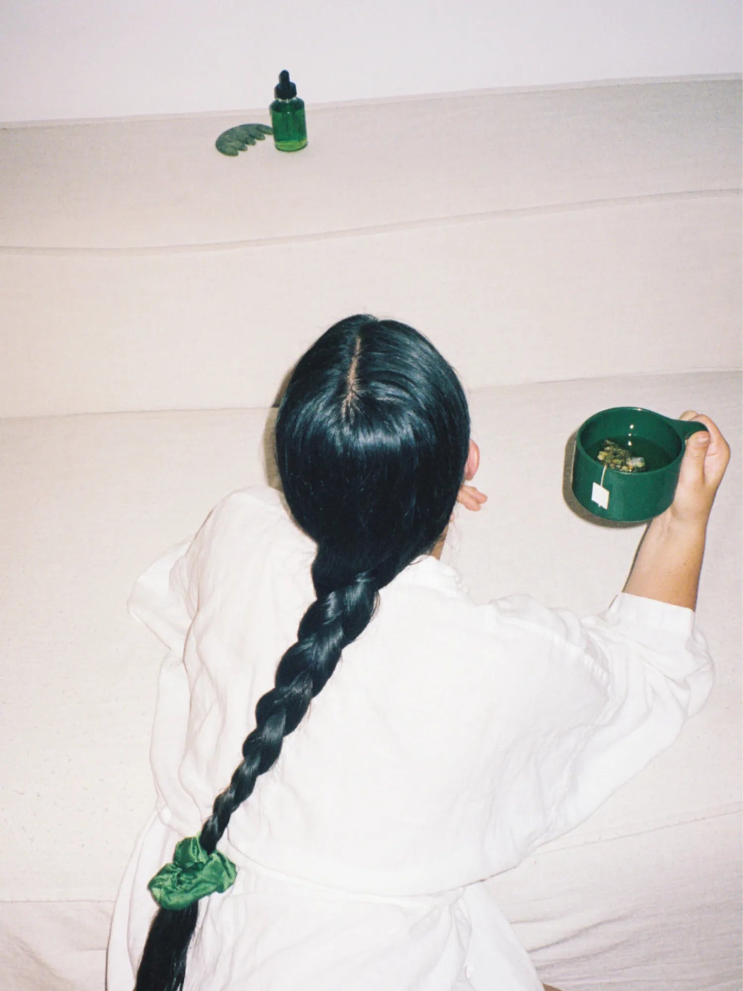 Rear view of a woman holding the green HINU Ritual Mug beside her braid