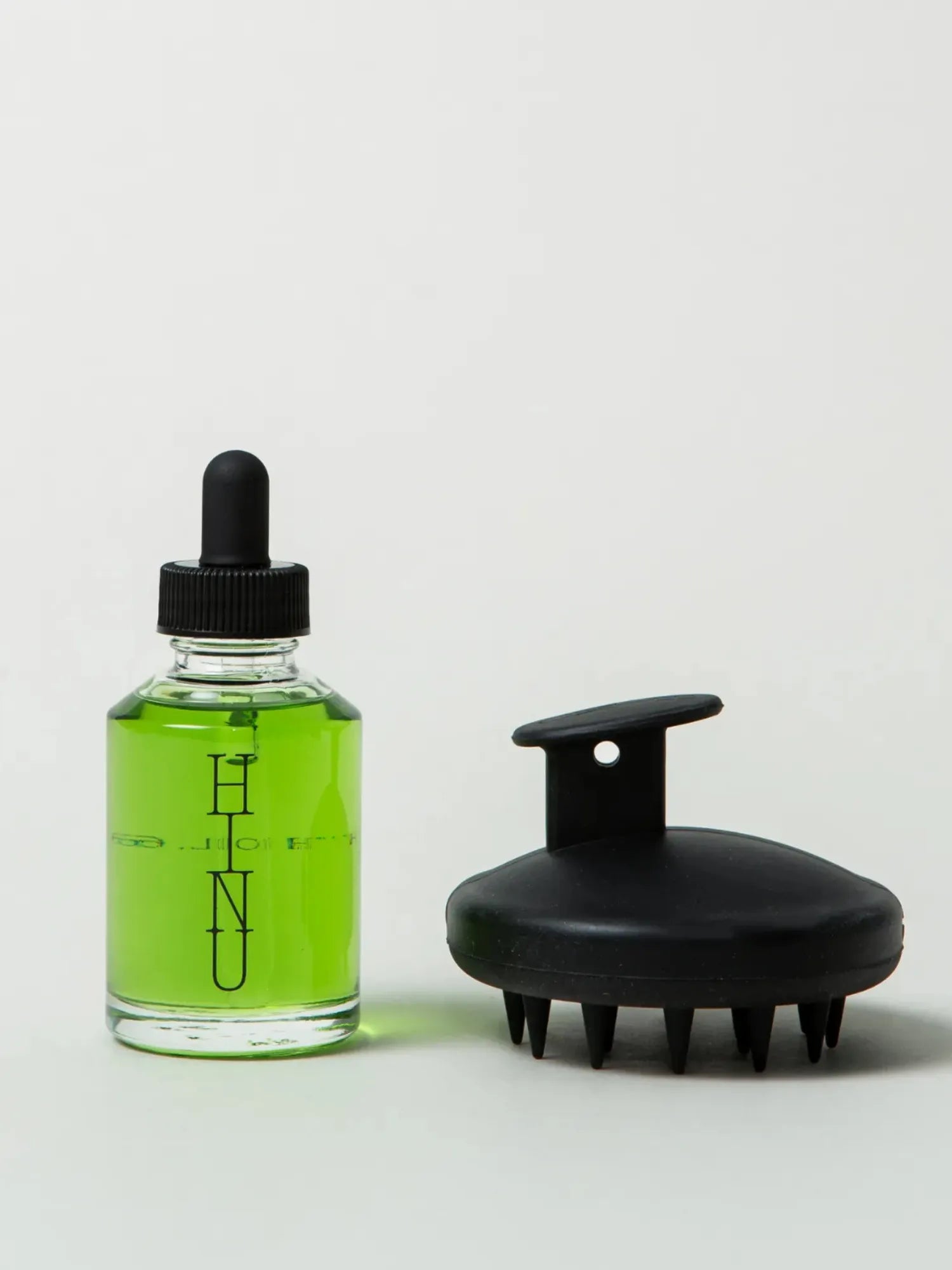 HINU Hair Growth Oil bottle beside the black Scalp Massager