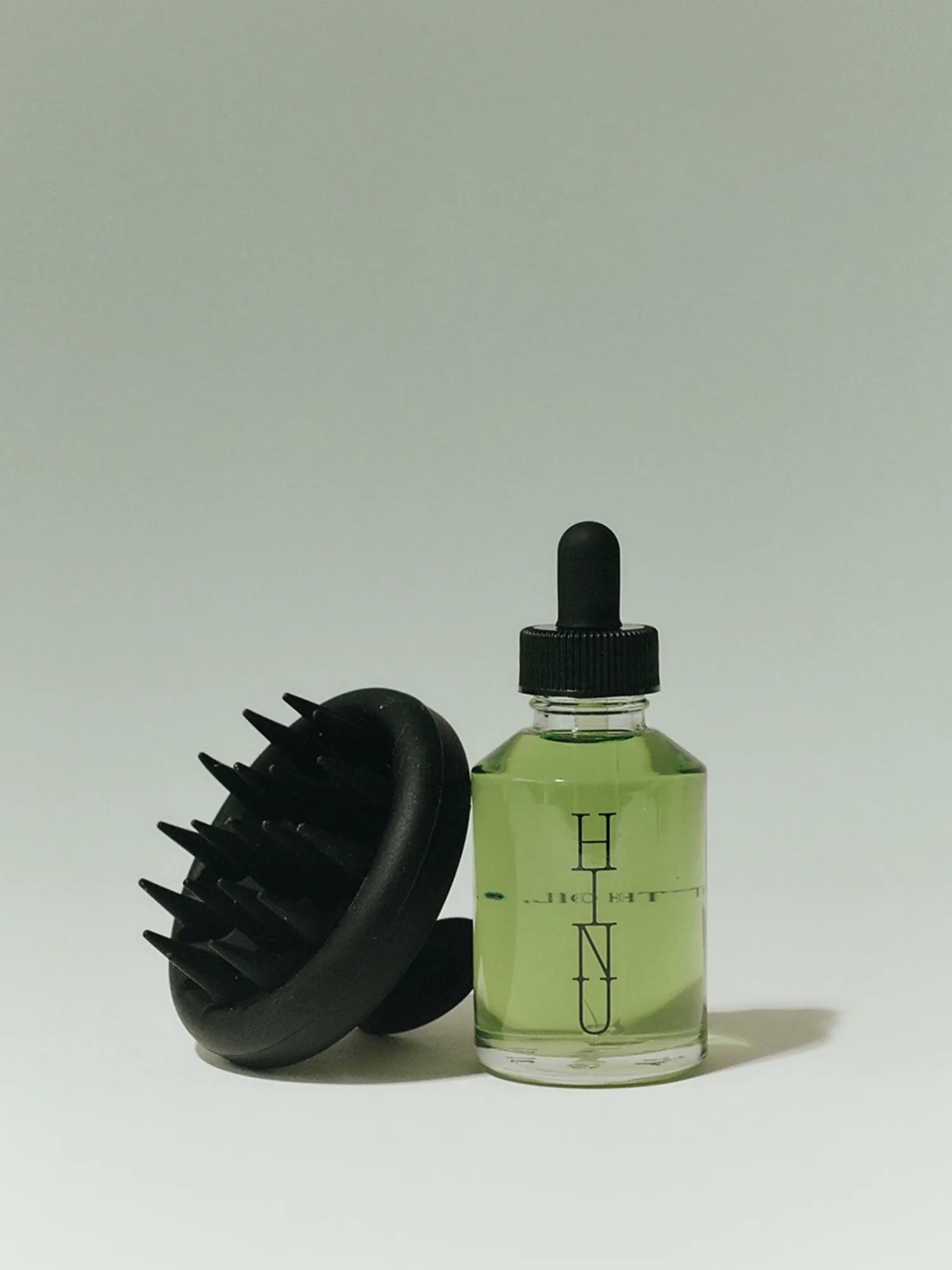 HINU Scalp Massager leaning beside a bottle of Hair Growth Oil
