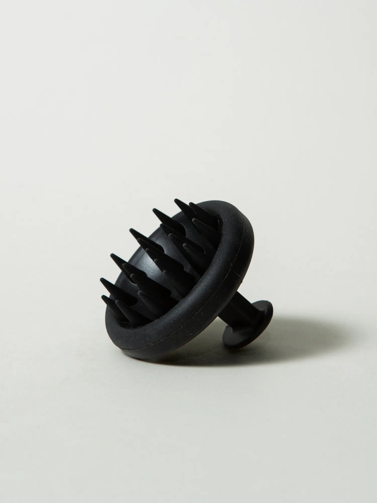 Angled view of the HINU Scalp Massager showing its bristles and hand loop