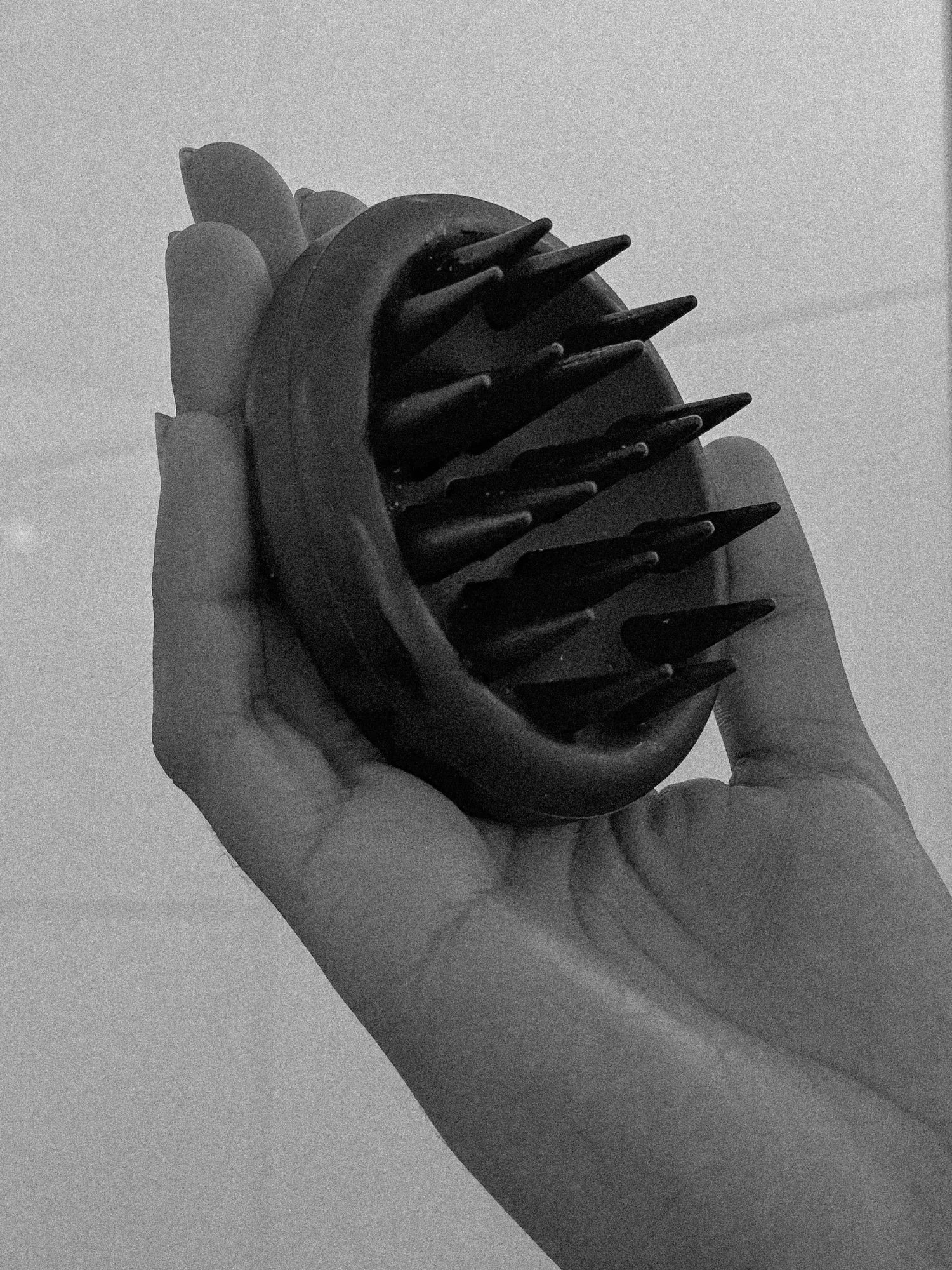Black-and-white close-up of the HINU Scalp Massager held in a hand
