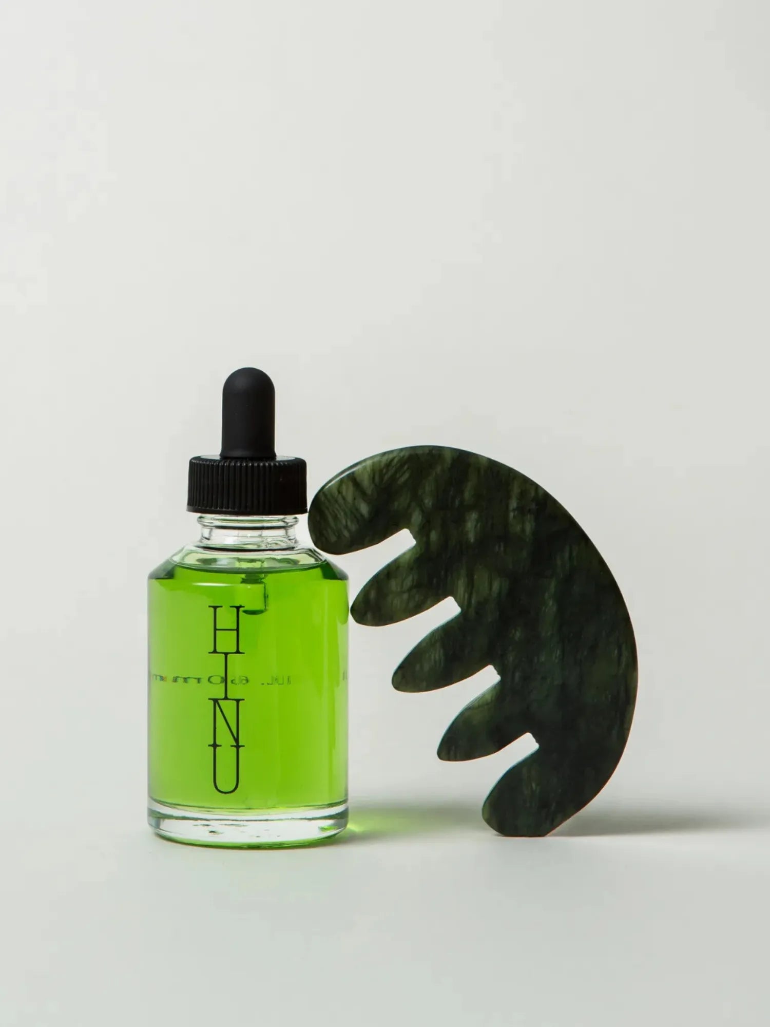 HINU Hair Growth Oil bottle beside the green Jade Scalp Stimulator