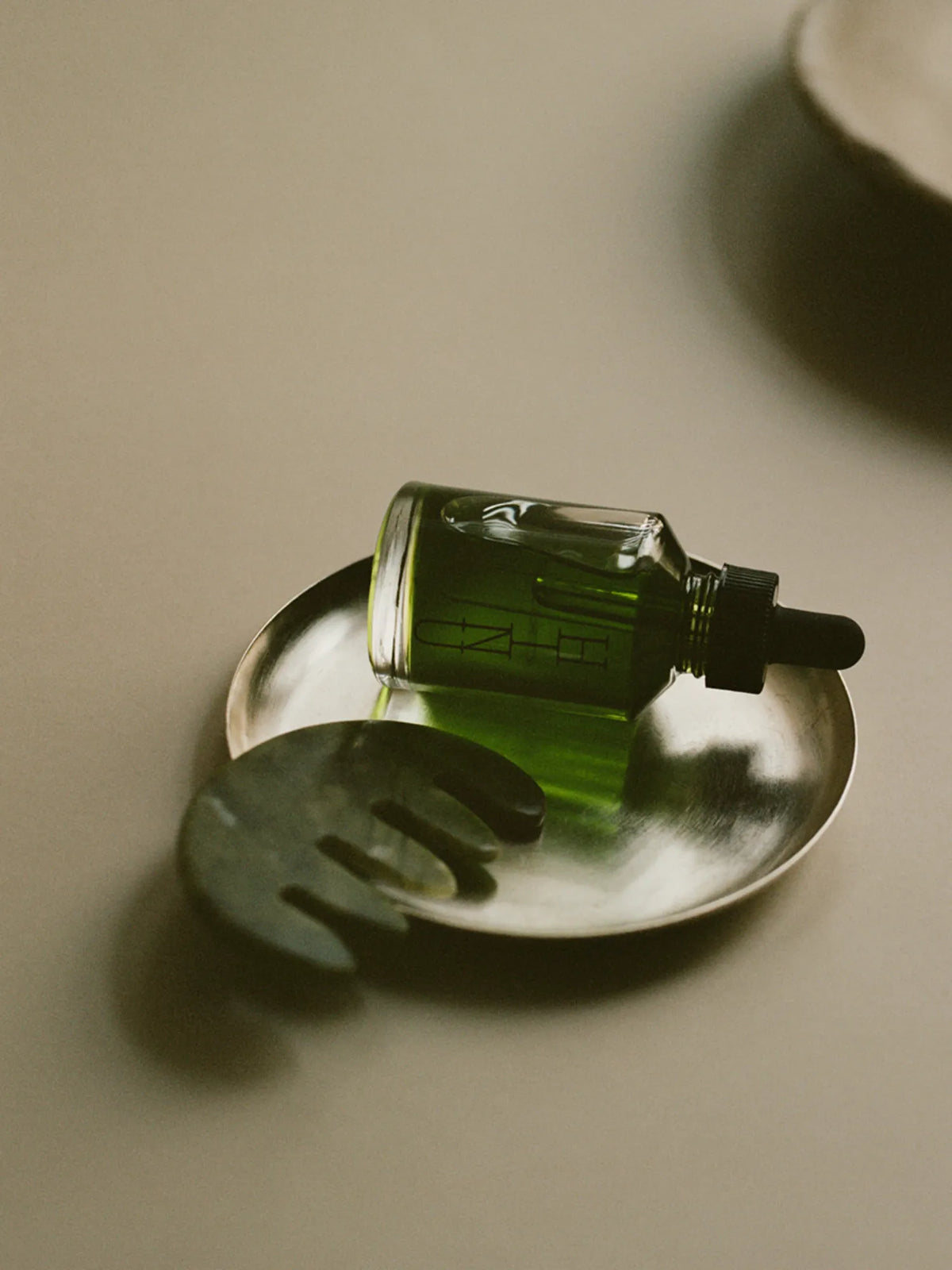 HINU Hair Growth Oil and jade tool reflected beside a metal dish