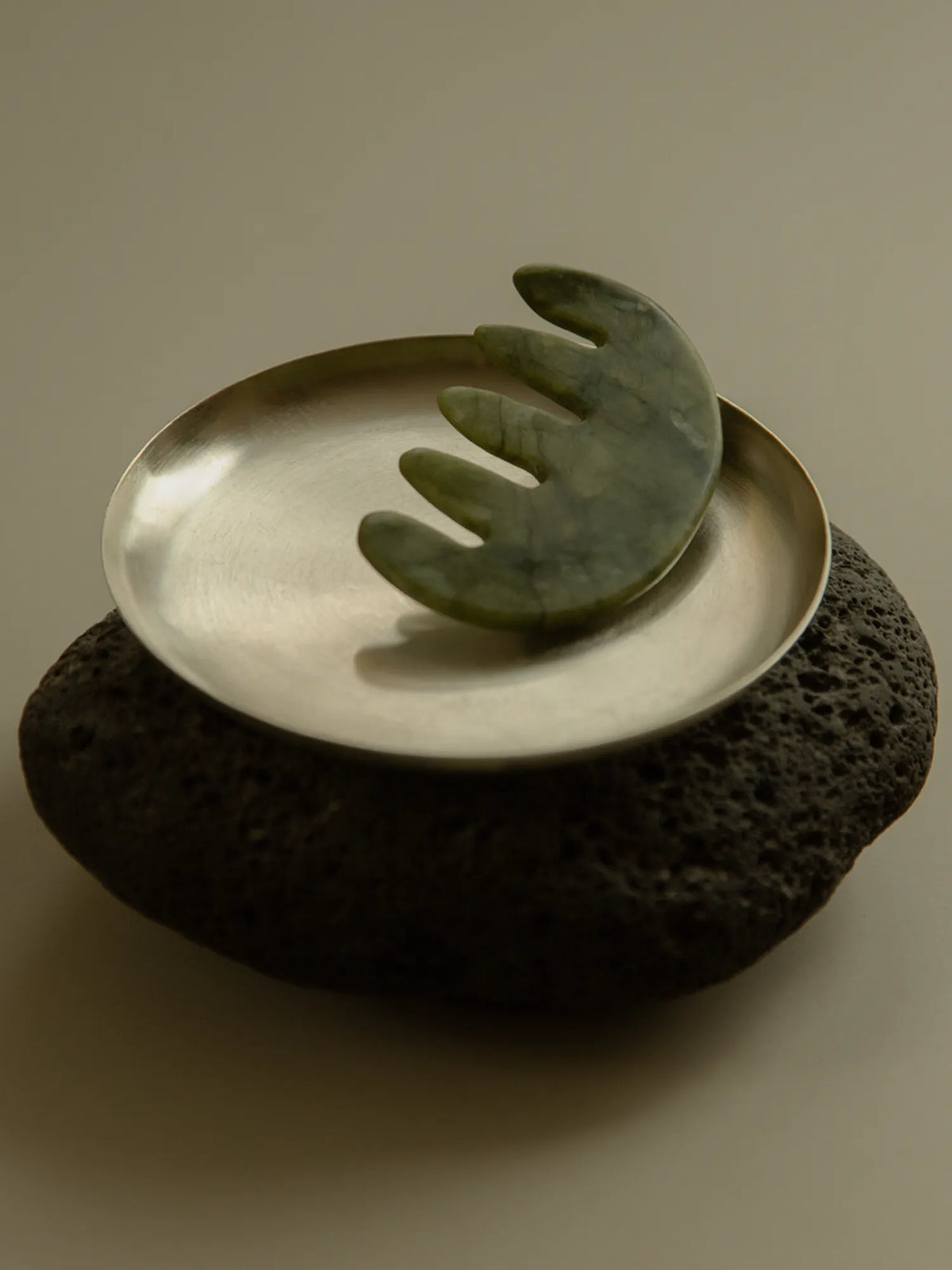 HINU Jade Scalp Stimulator displayed in a metal dish on a dark stone base