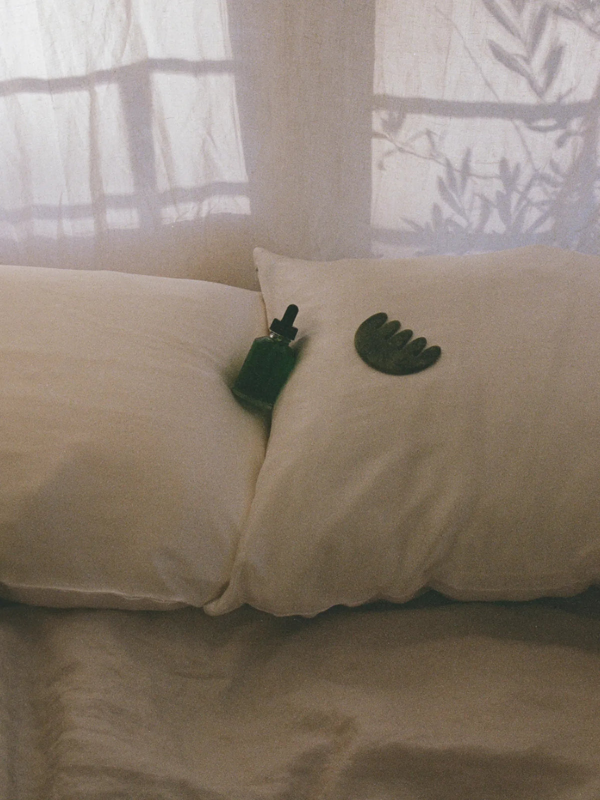 HINU Hair Growth Oil and jade tool arranged on a white cushion