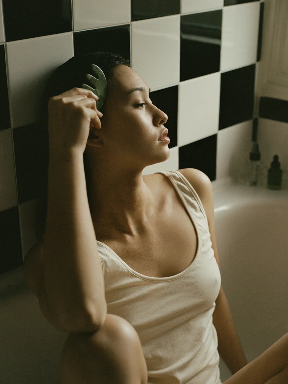 Woman using the HINU Jade Scalp Stimulator at her temple in a bathroom