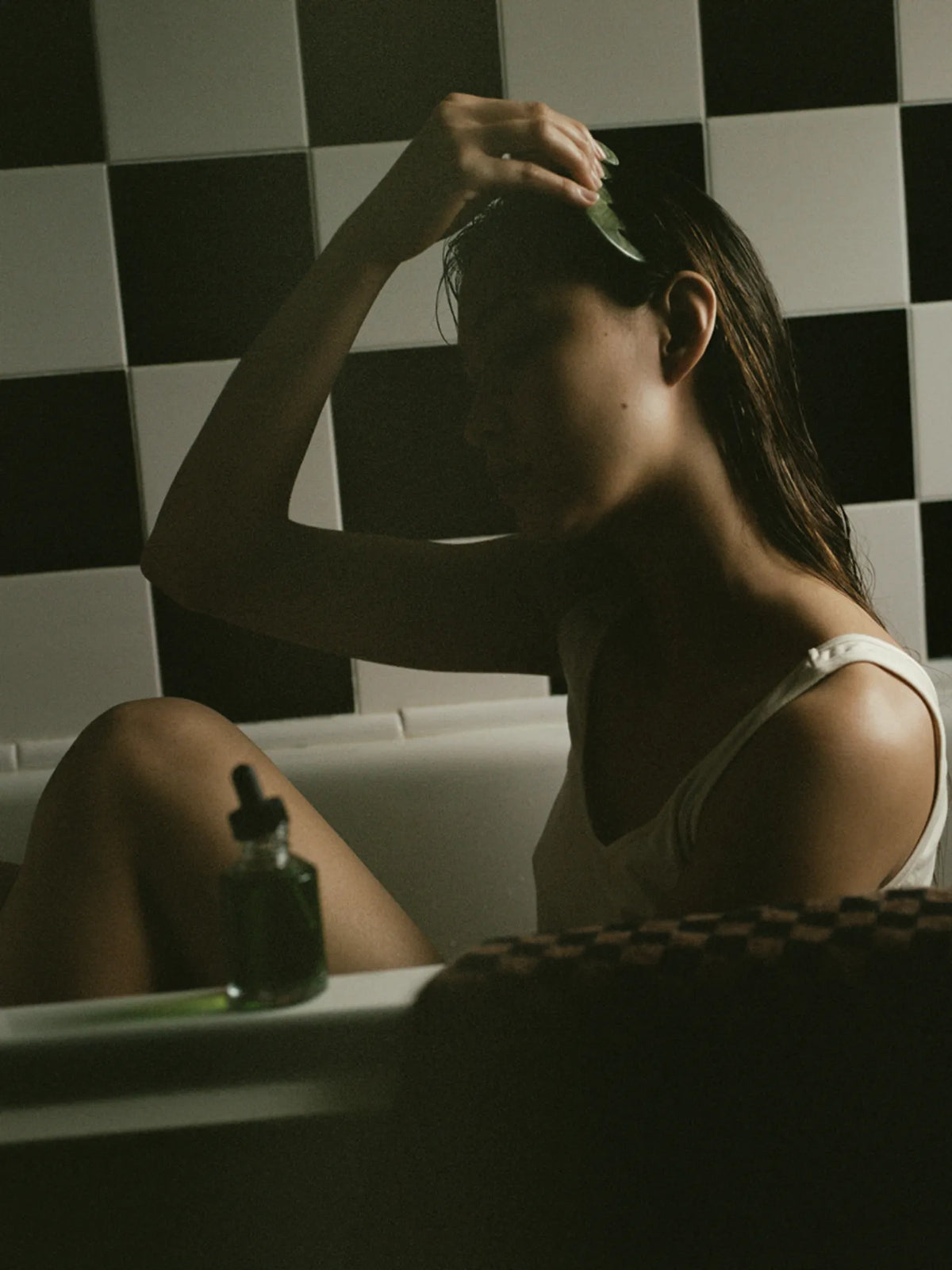 Woman holding the HINU Jade Scalp Stimulator to her forehead beside a bath
