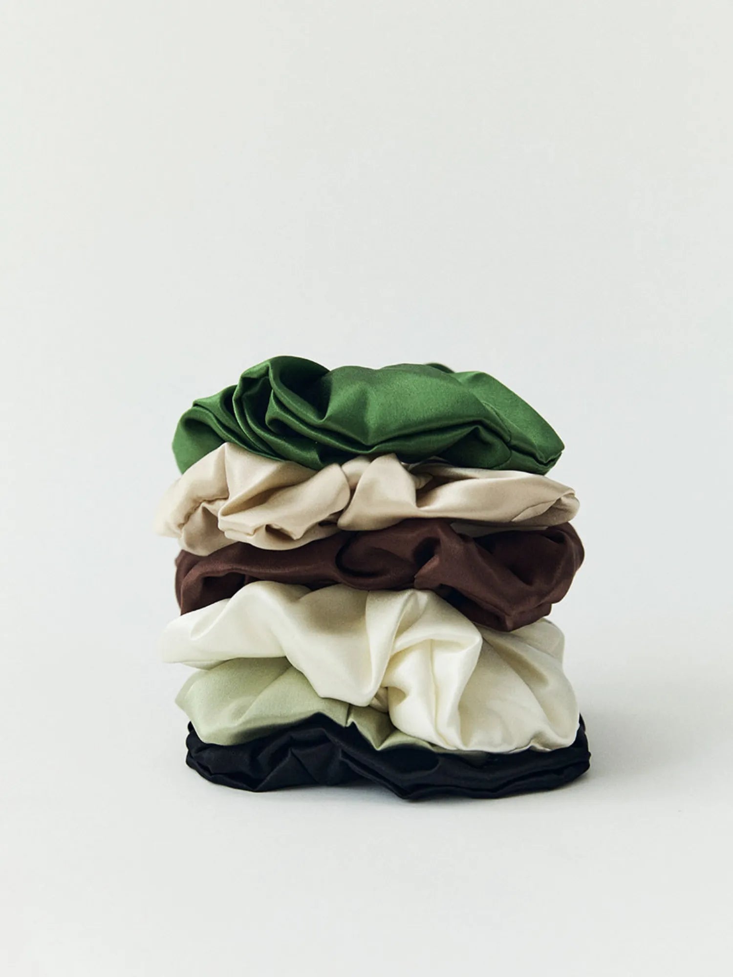 Stack of HINU Silk Scrunchies in green, cream, brown, oat and black